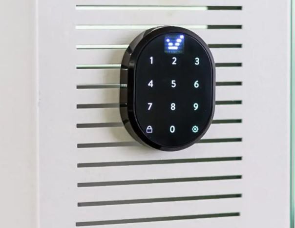Serratura digitale a tastiera nera montata su un pannello della porta bianco con fessure.