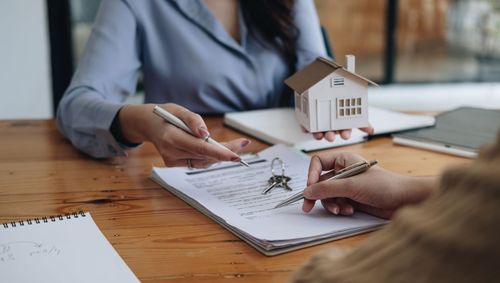 Two people reviewing a house model and papers at a wooden table