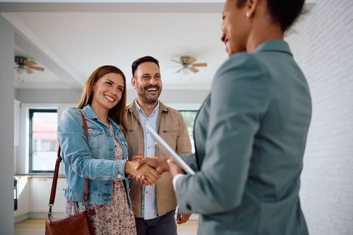 Two people shake hands with a realtor in a bright living room during a home viewing.