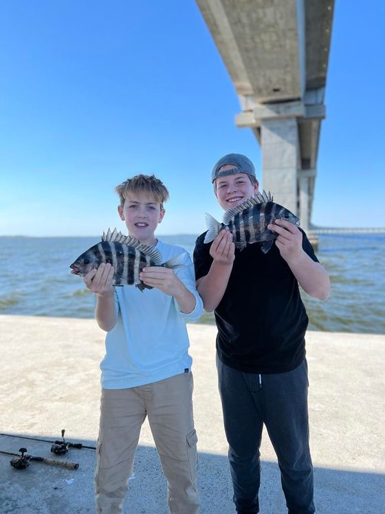 Two young boys are holding fish in front of a bridge.