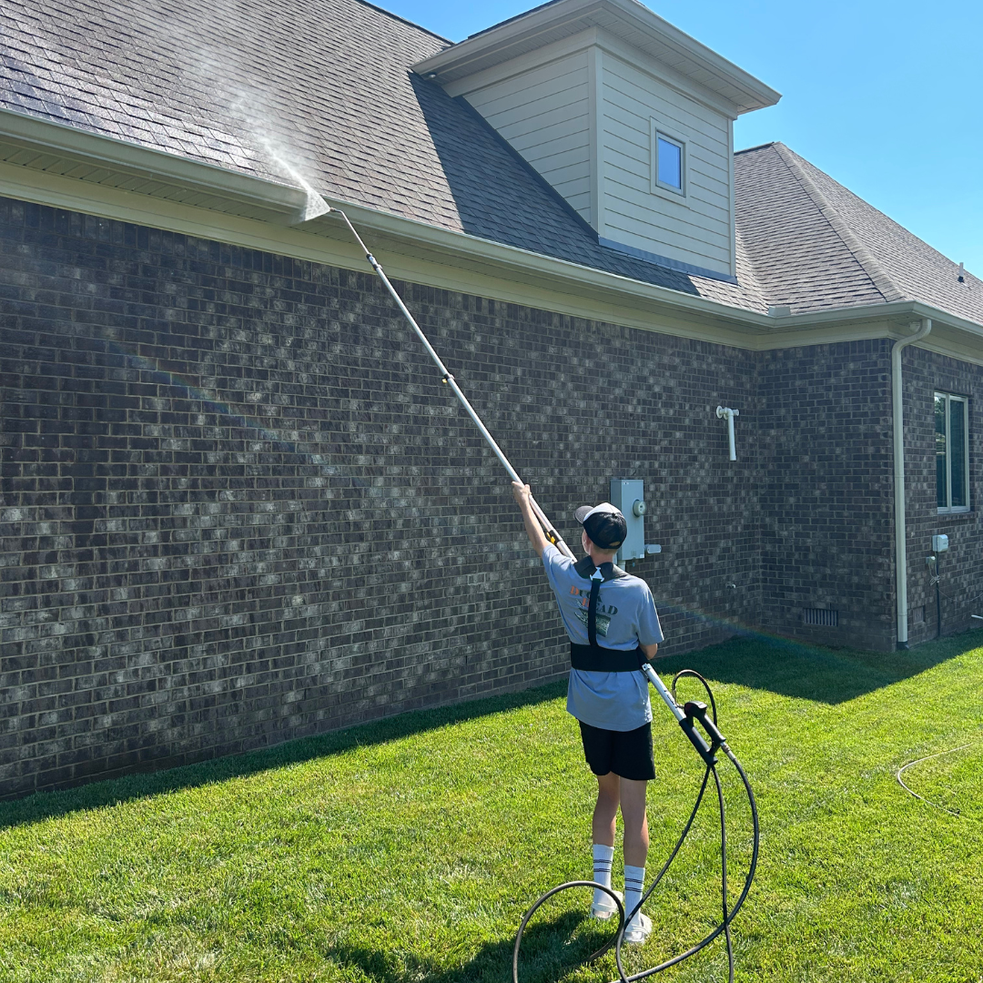 A man is cleaning the roof of a brick house with a high pressure washer.