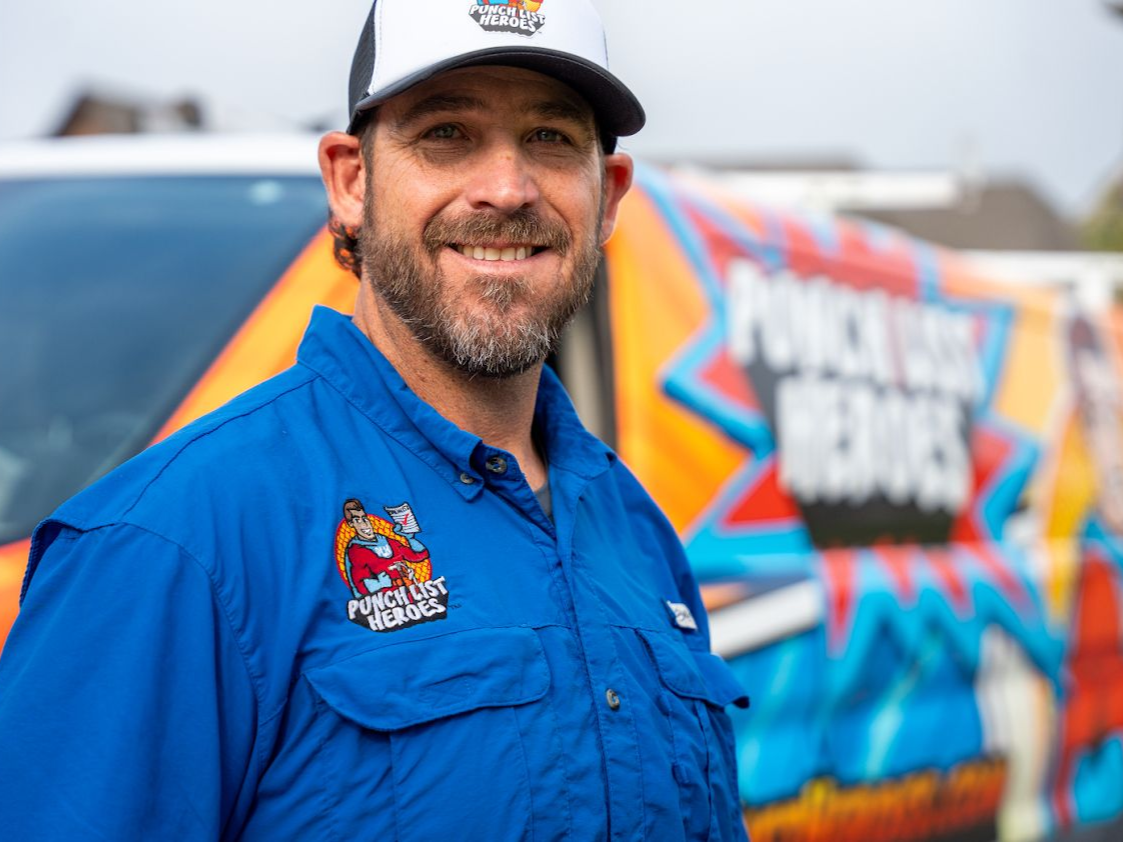 A man in a blue shirt and hat is standing in front of a van. A man in a blue shirt and hat is standing in front of a van.
