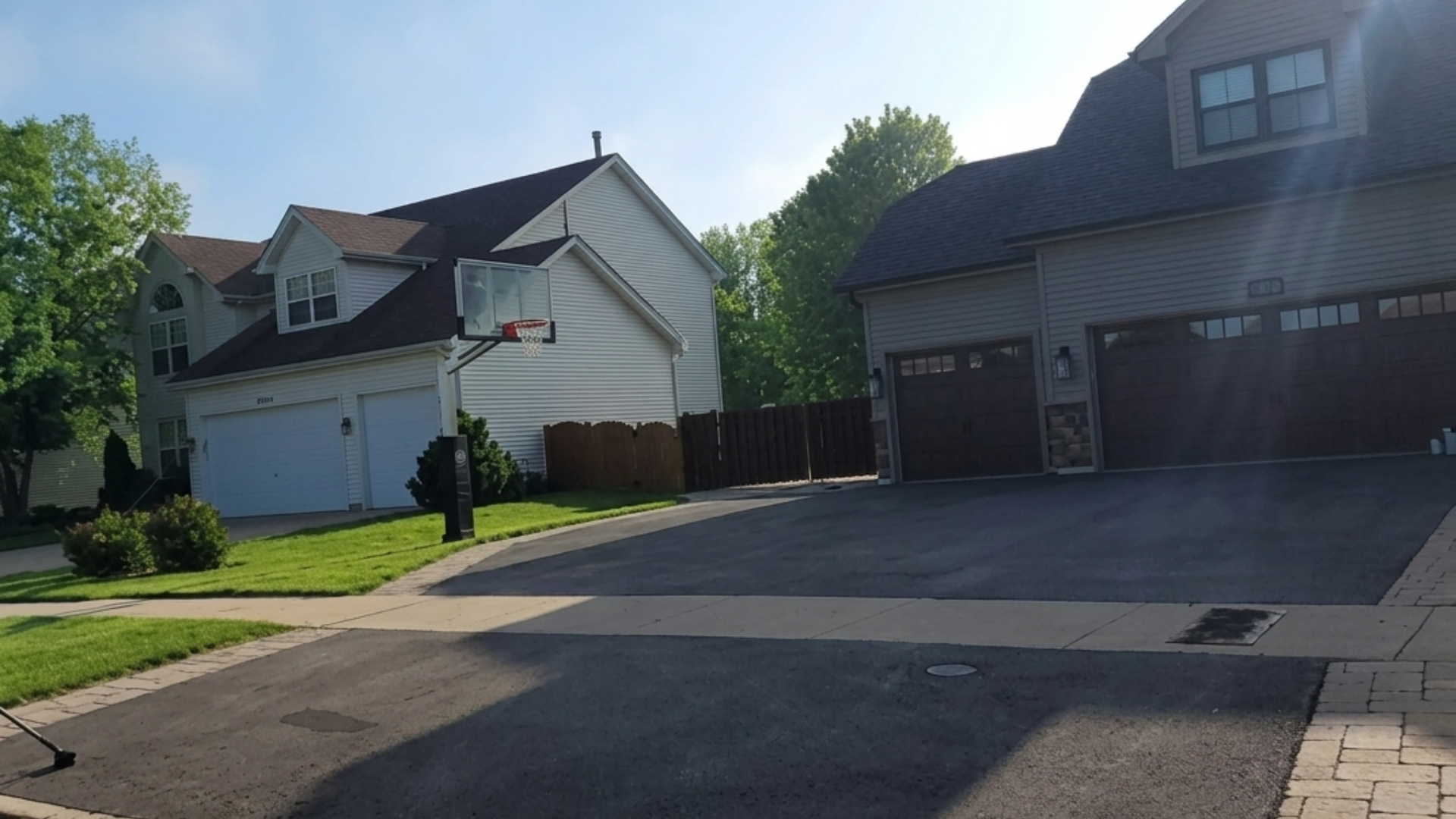 Suburban street with two houses, garages, driveway, and green lawn in bright sunlight