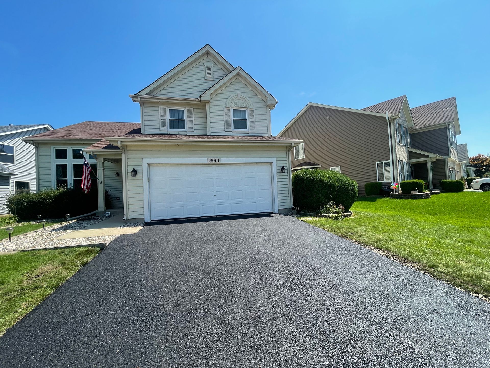 Suburban two-story house with a white garage, black driveway, and lawn in front