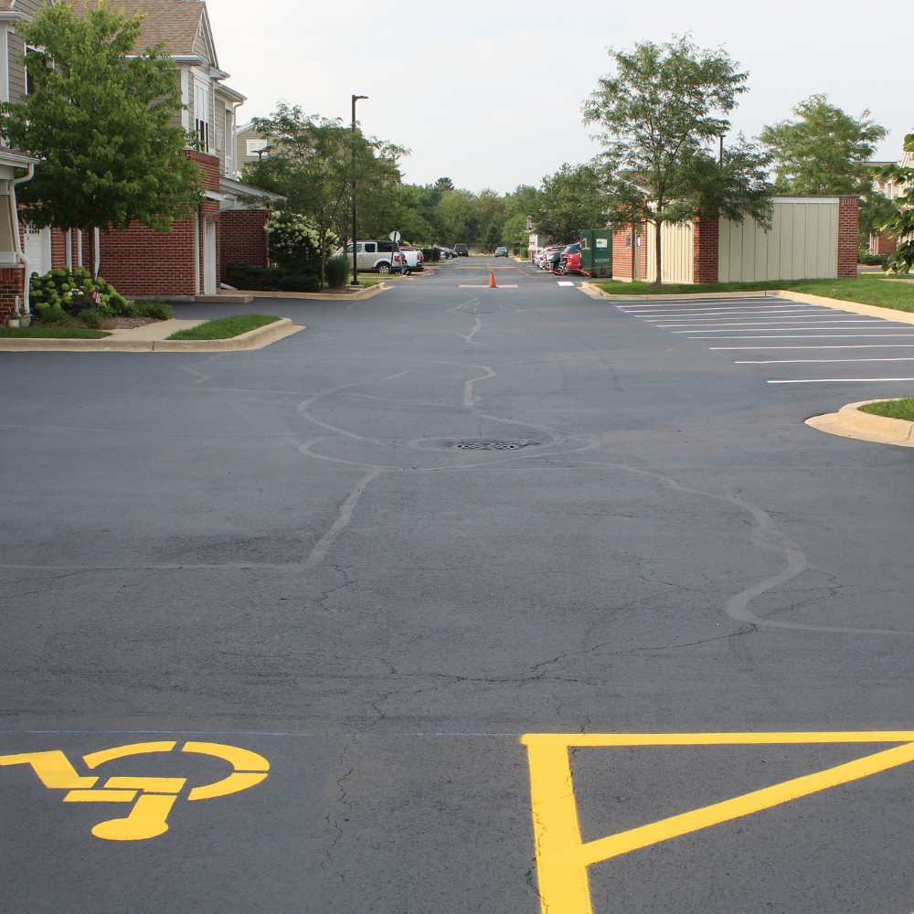Suburban house with a two-car garage and a freshly paved dark driveway on a sunny day