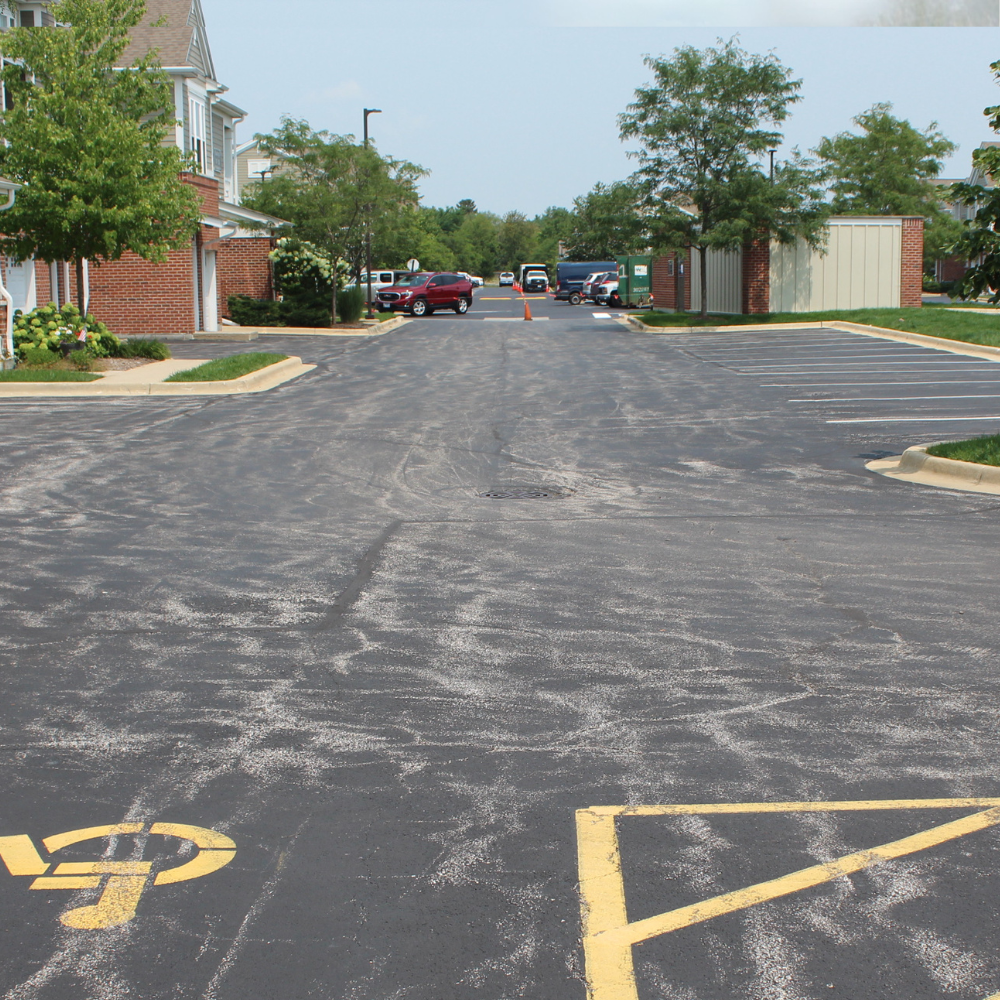Residential driveway resurfaced with dark asphalt in front of two beige suburban garage doors