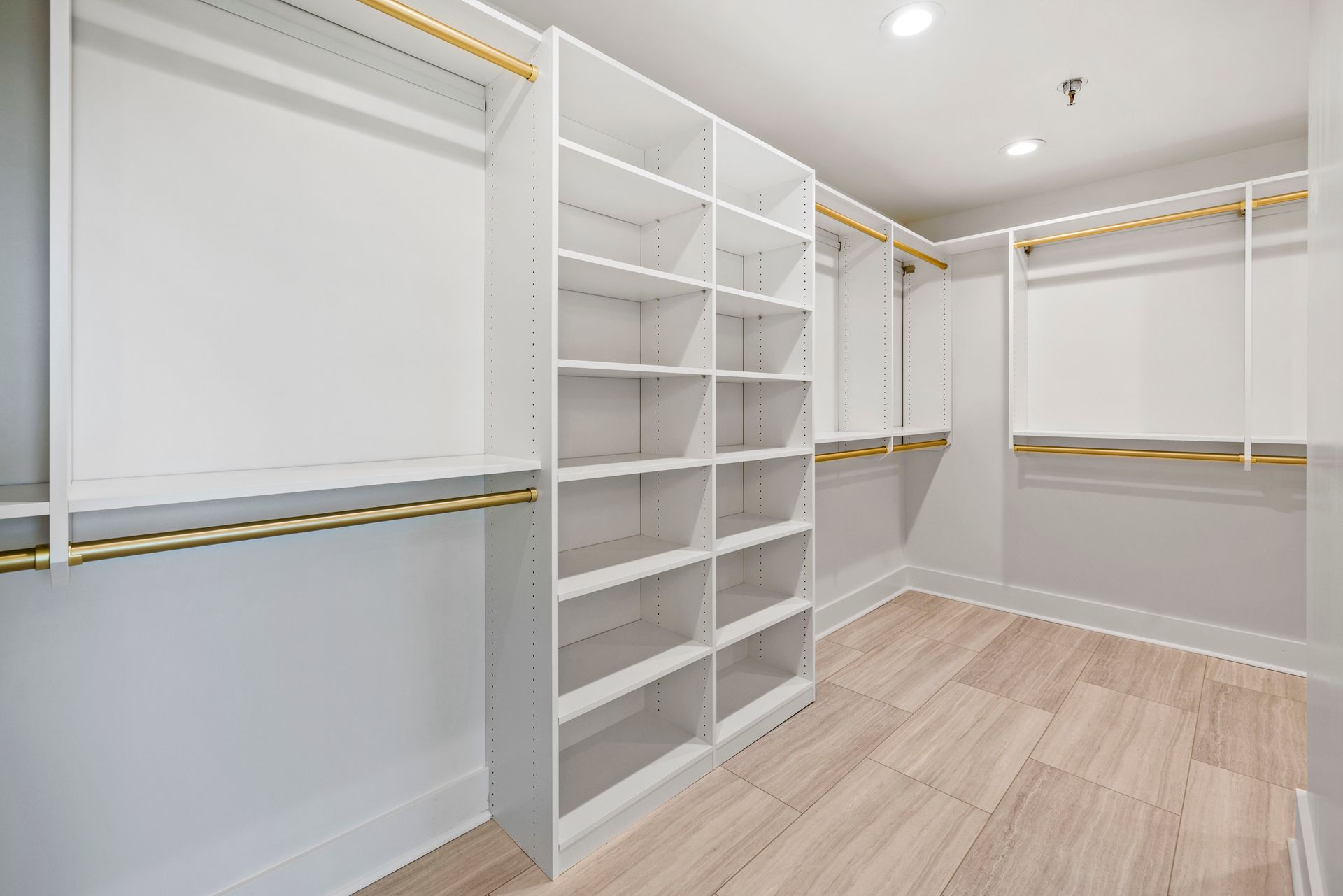 Empty white walk-in closet with shelves, clothing rods, and light wood flooring.