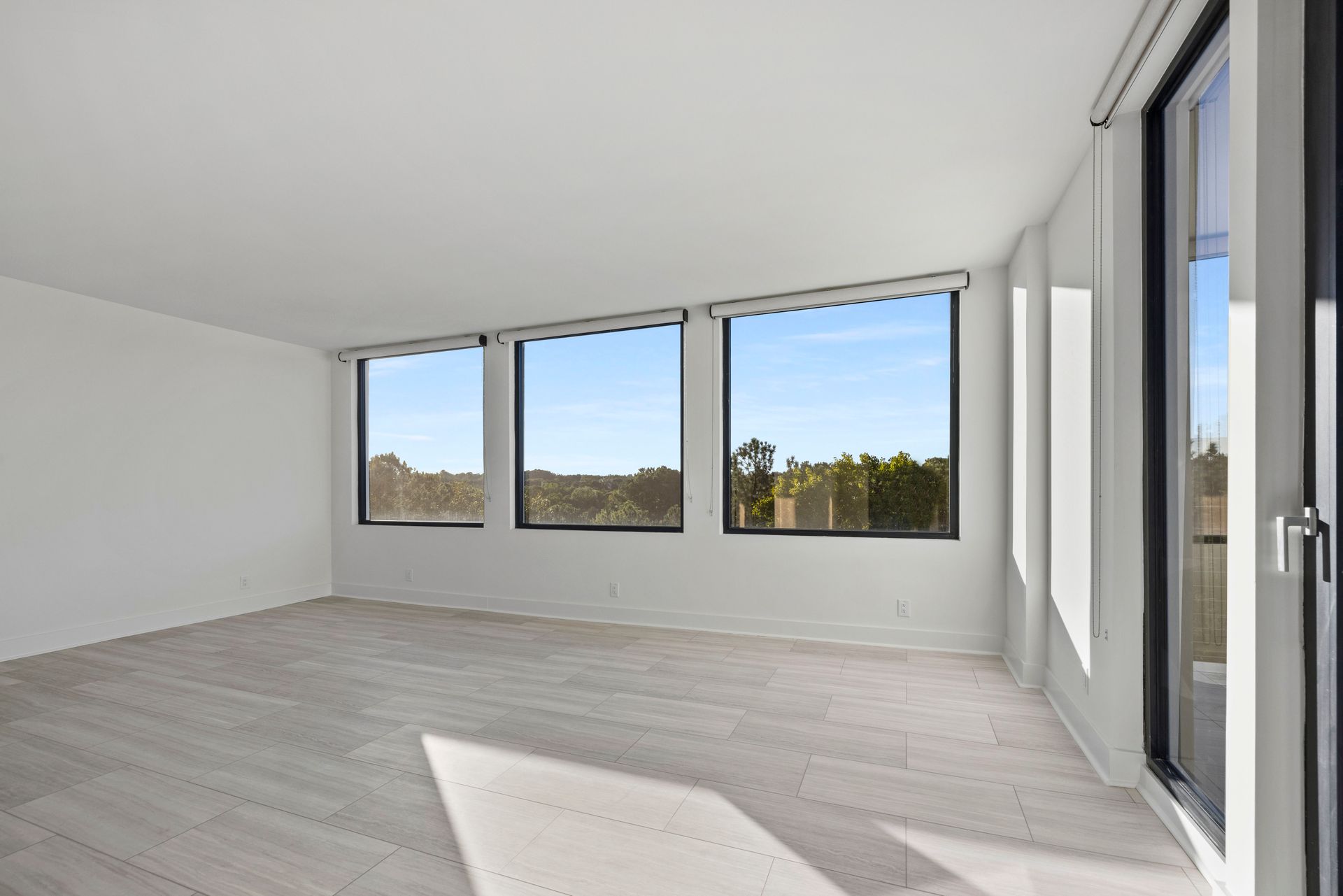 Empty room with large windows, bright white walls, light flooring, and a view of the sky.