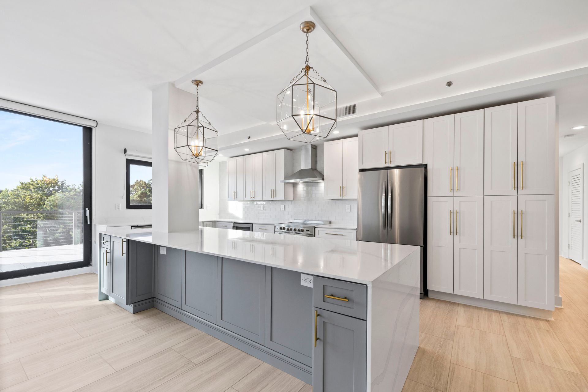 Modern kitchen with gray island, white cabinets, stainless steel appliances, and large windows.