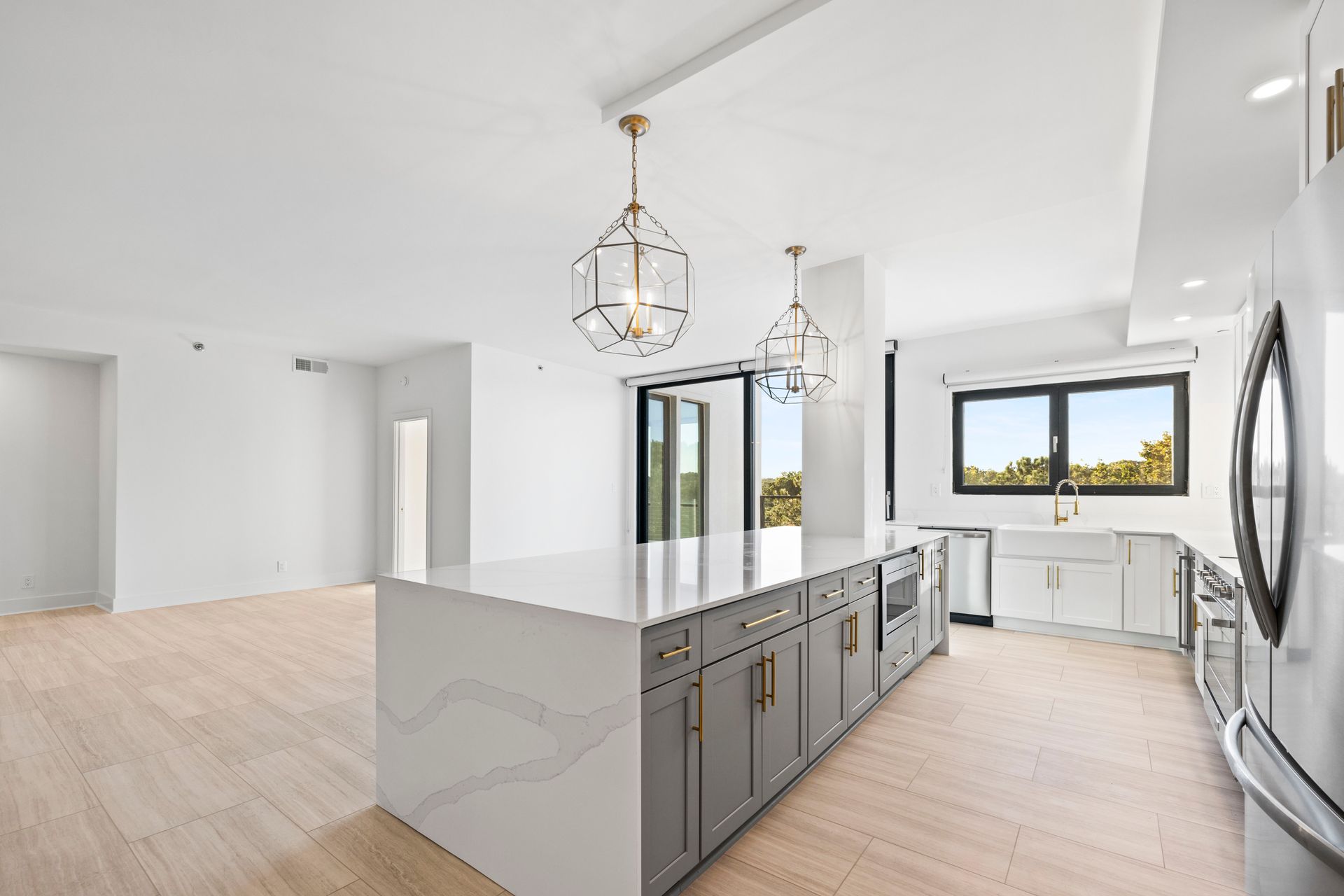 Modern kitchen with gray island, light wood floor, white walls, and hanging pendant lights.