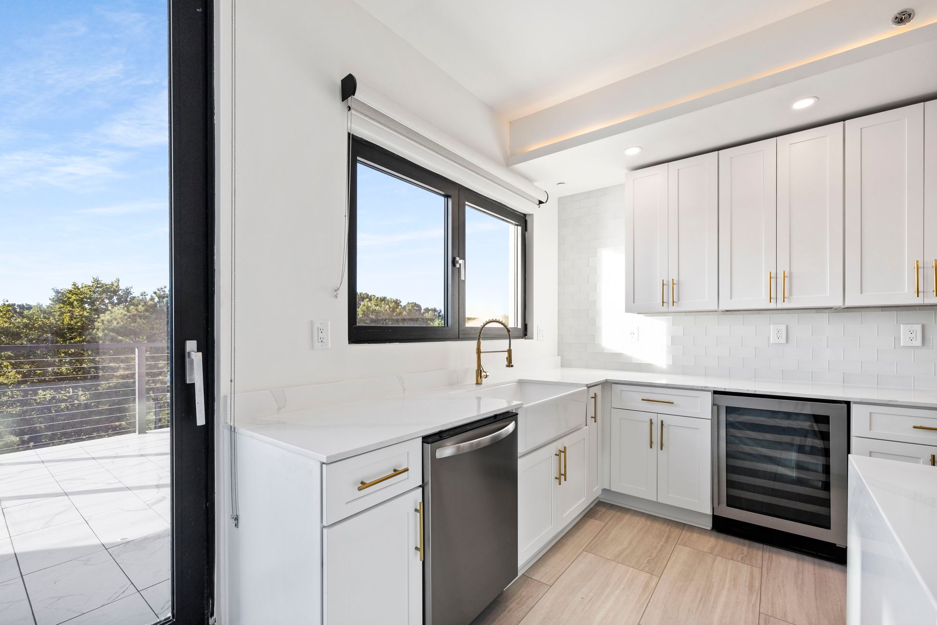 Modern white kitchen with stainless steel appliances, a window, and wood flooring.
