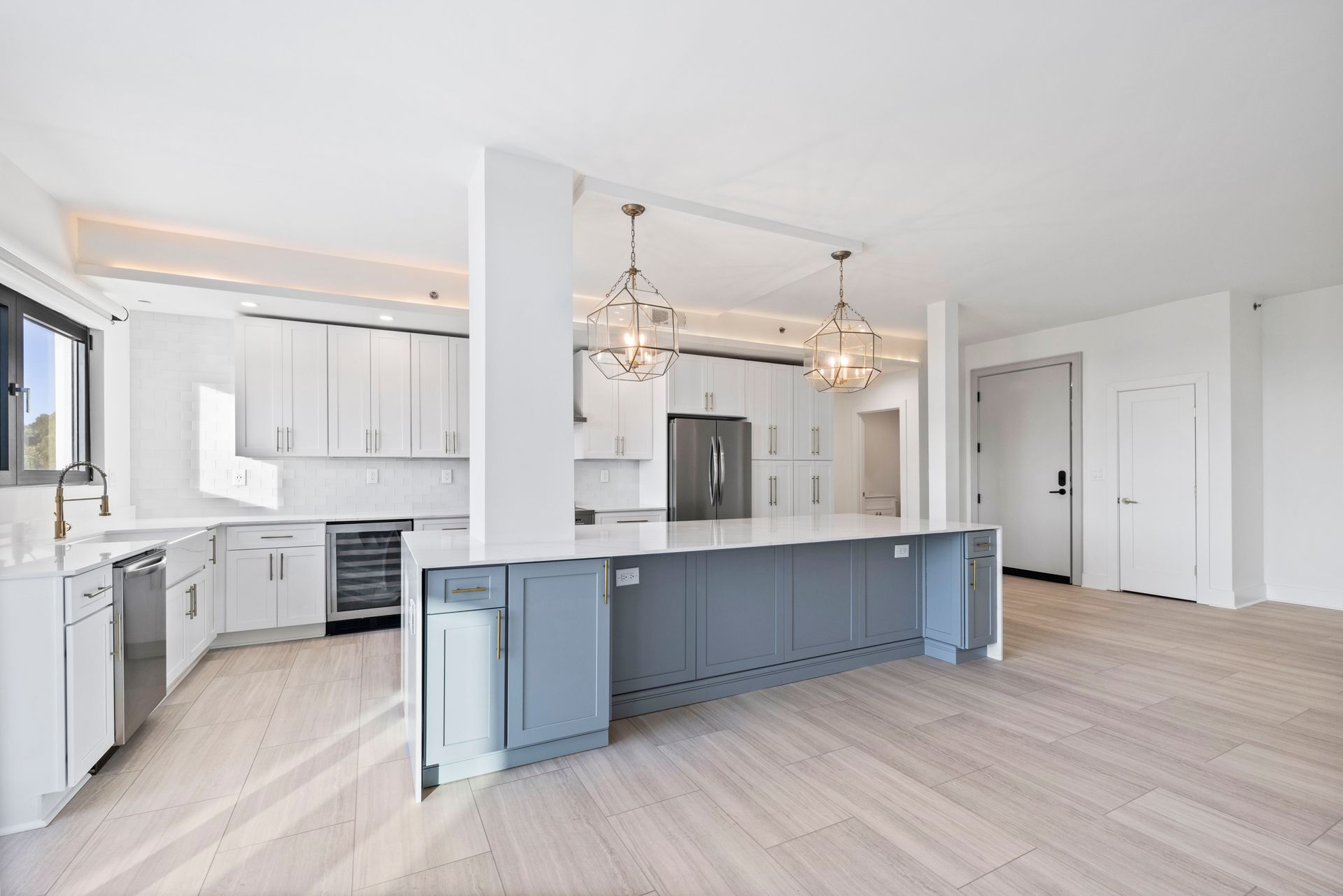 Modern white kitchen with a gray island, stainless steel appliances, and two pendant lights.