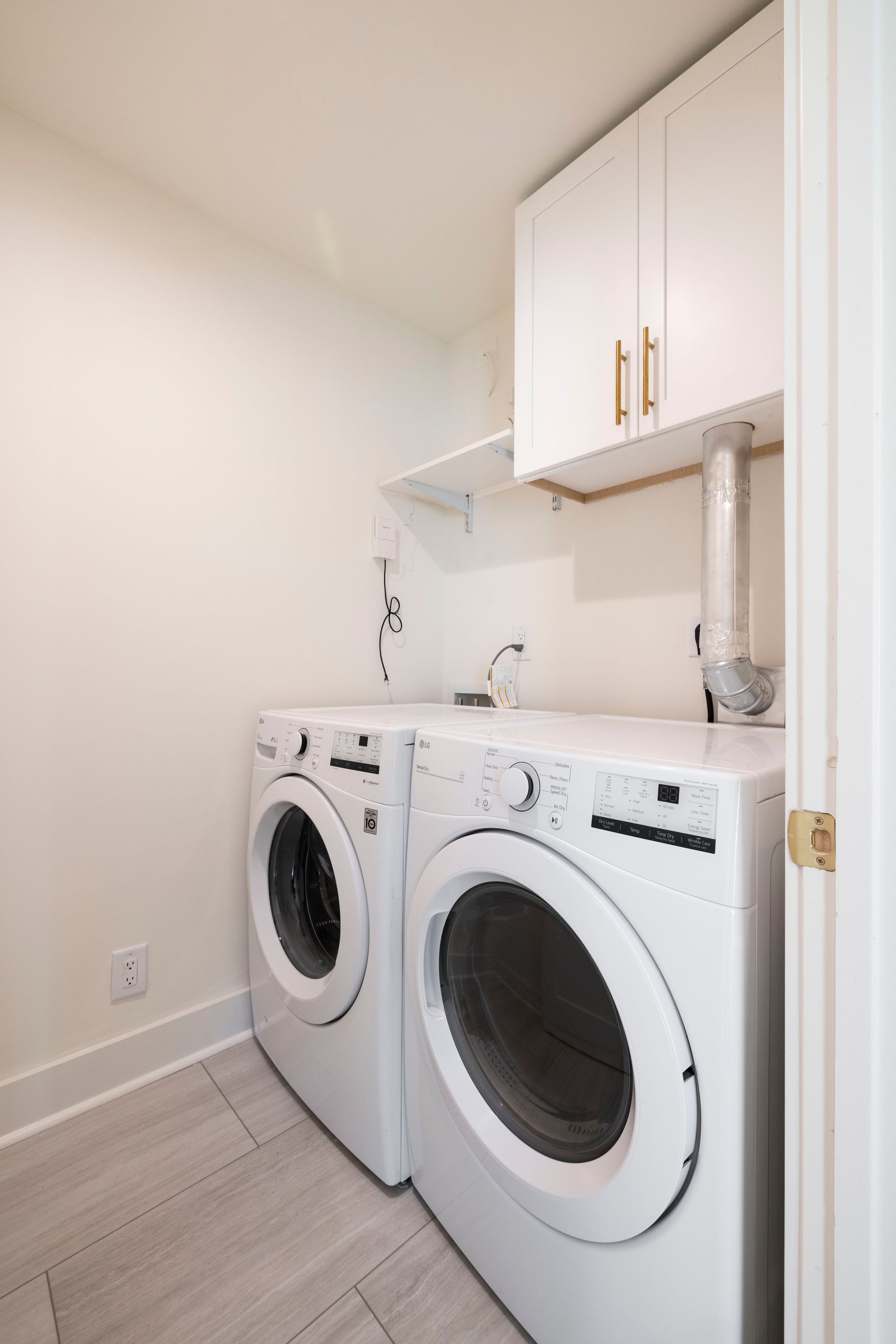 Laundry room with white washer and dryer, cabinets, and a vent.