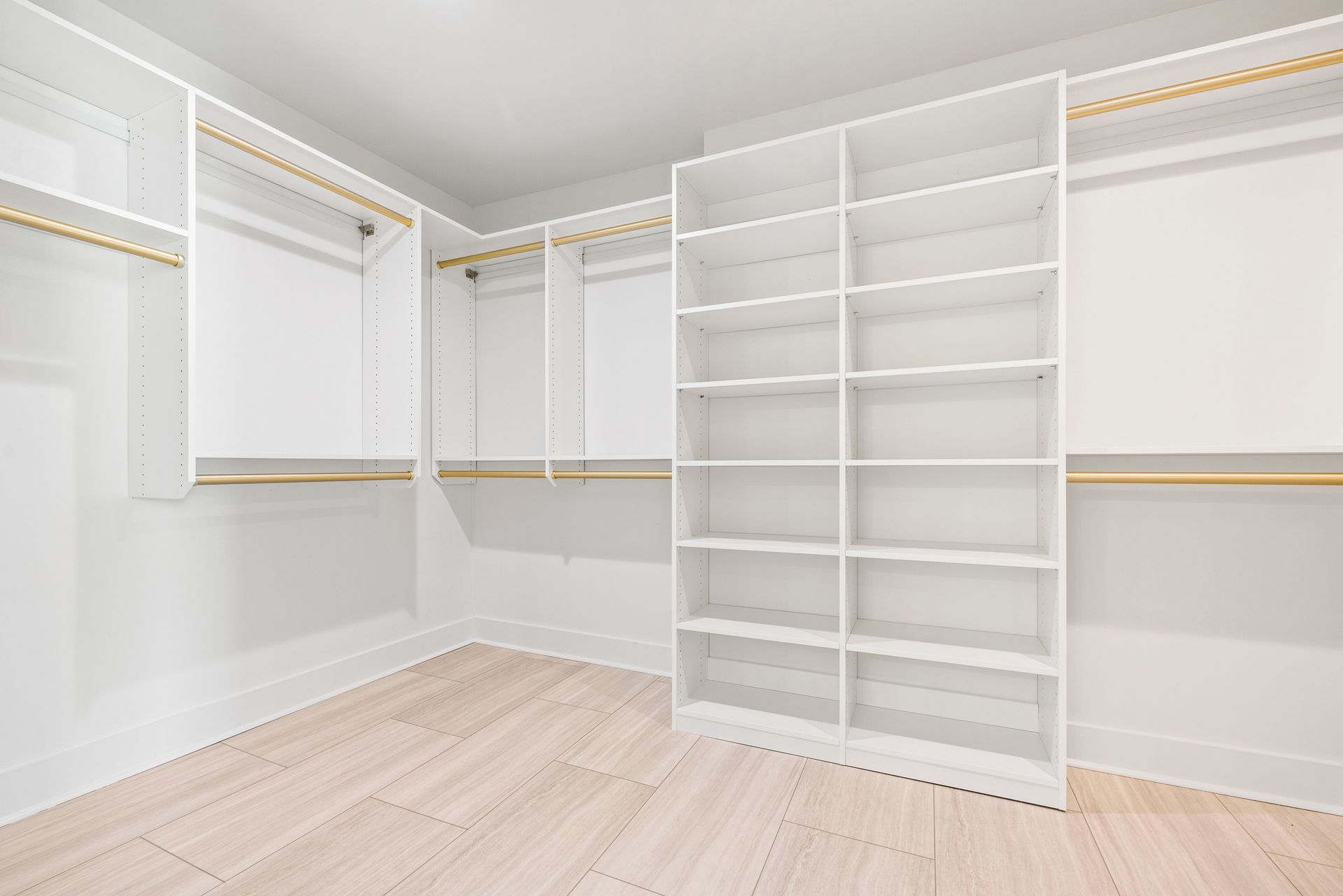 Empty white closet with shelving, drawers, and hanging rods. Light wood floors.