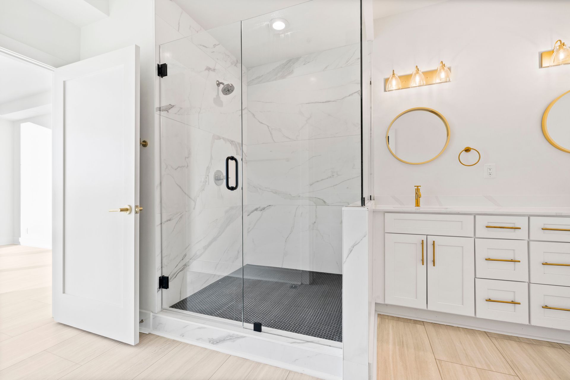 Modern white bathroom with marble shower, gold fixtures, and double vanity.