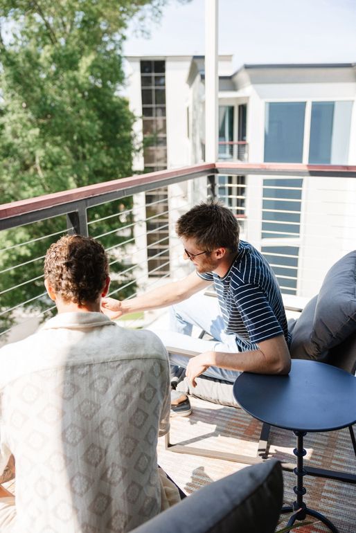 Two men are sitting on a balcony talking to each other.