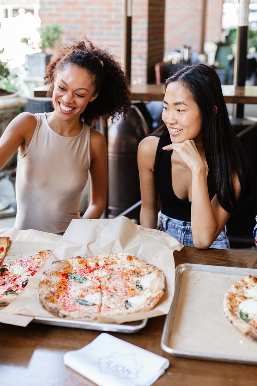Two women are sitting at a table eating pizza.