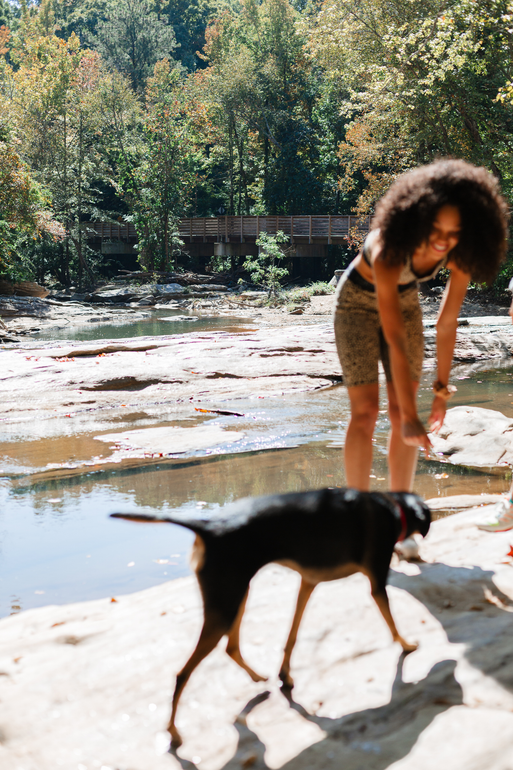 A woman is standing next to a dog on a beach near a river.