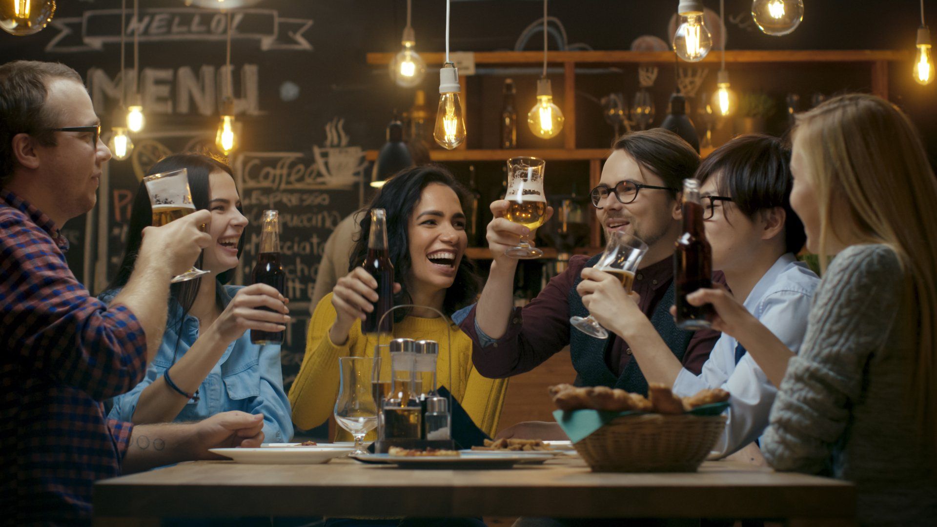 A group of people are sitting at a table in a restaurant toasting with beer.