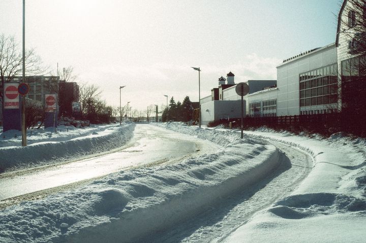 Snow-covered road curving past buildings and streetlights on a bright winter day