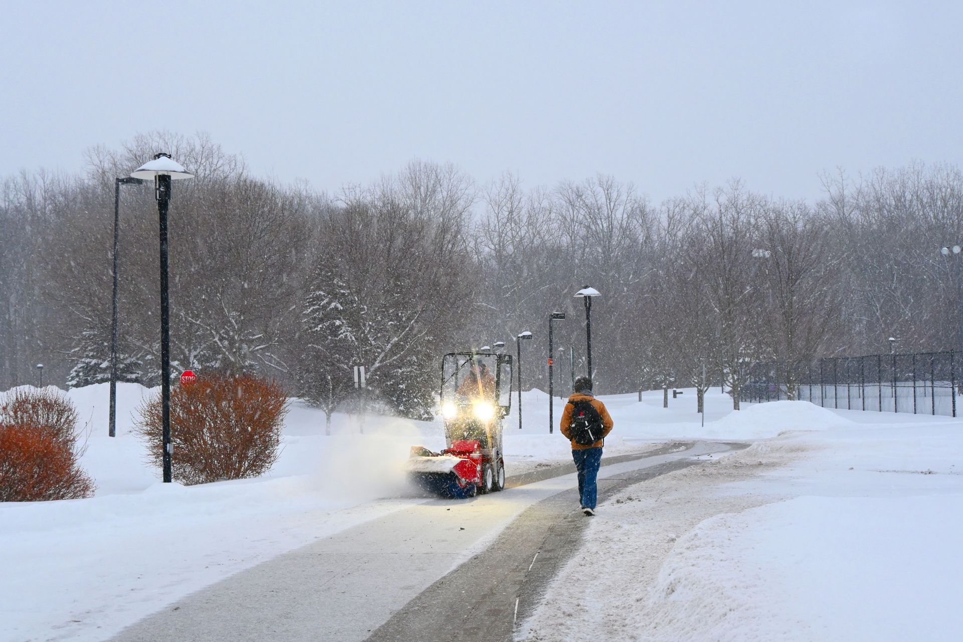 Snowy park path with a person walking past a small snowplow clearing the way