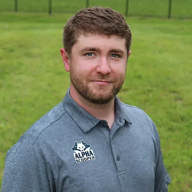 A man with a beard and a gray shirt is standing in a field.