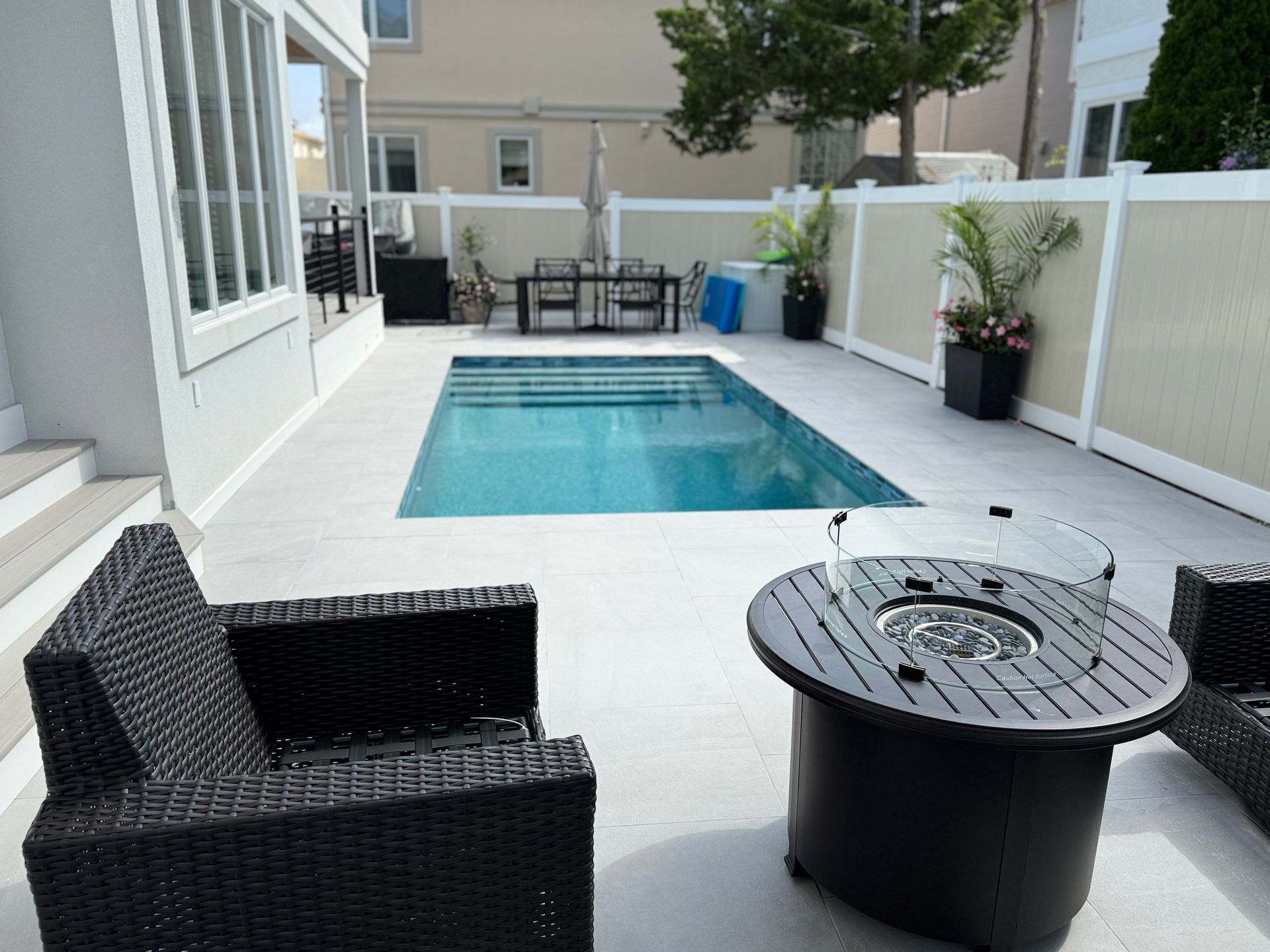 Backyard patio with a small rectangular pool, wicker chairs, and a round fire pit table