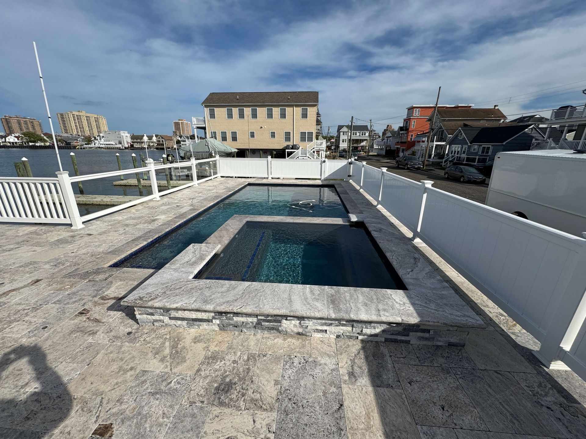 Rooftop deck with a rectangular pool, white railings, and oceanfront buildings in the background