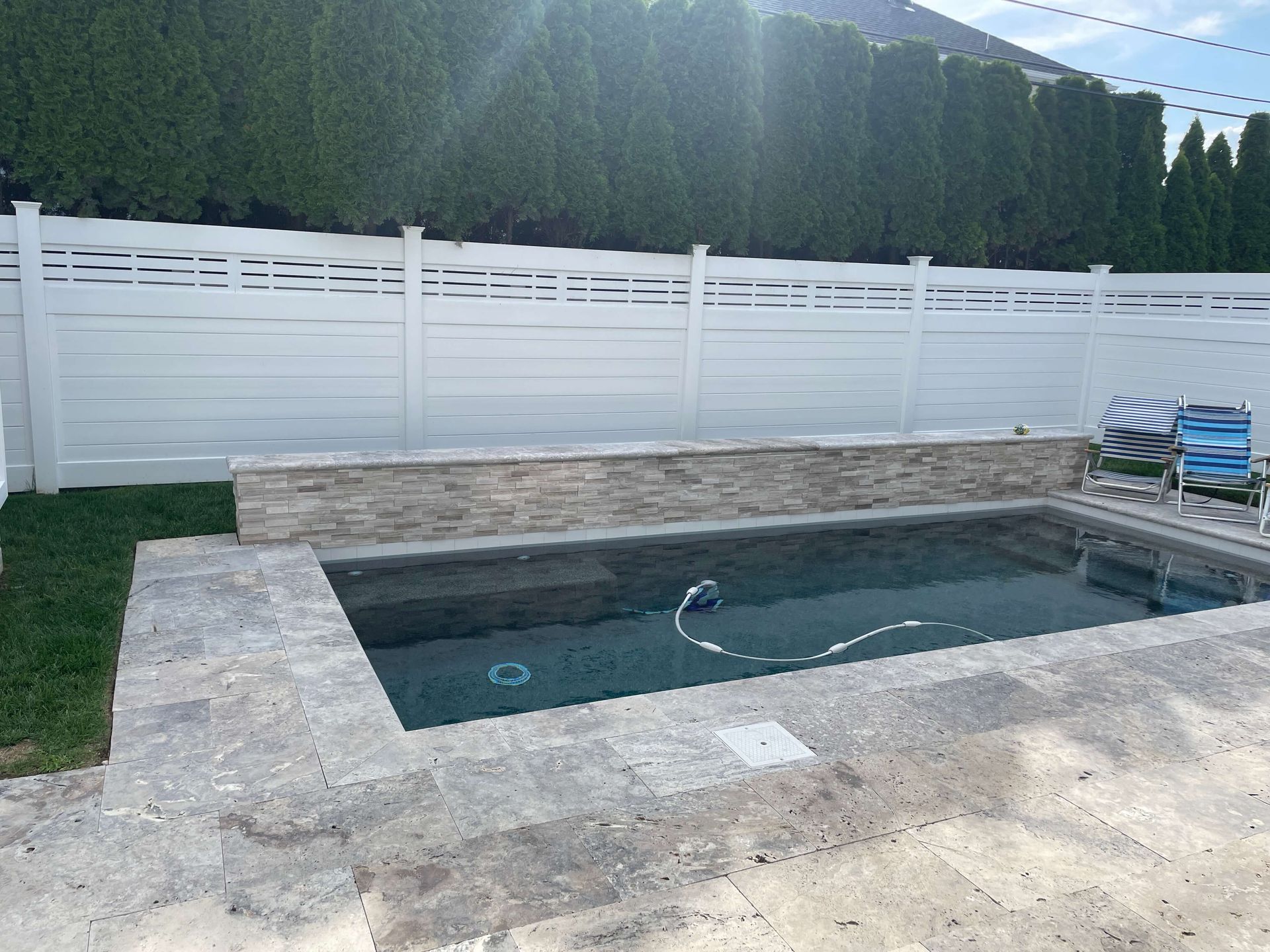 Concrete backyard pool with white fence and forest backdrop