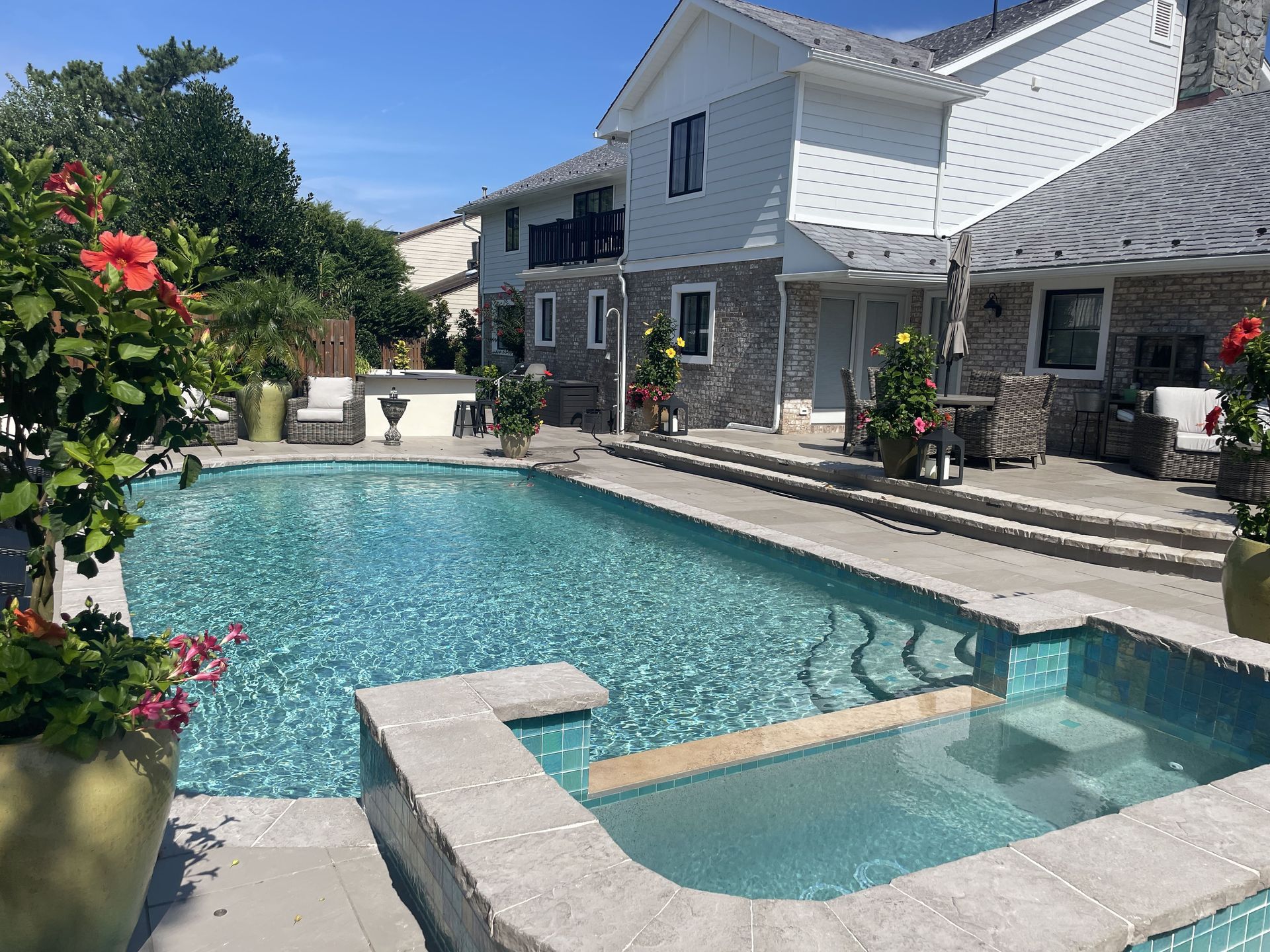 Backyard pool and hot tub beside a two-story house on a sunny day