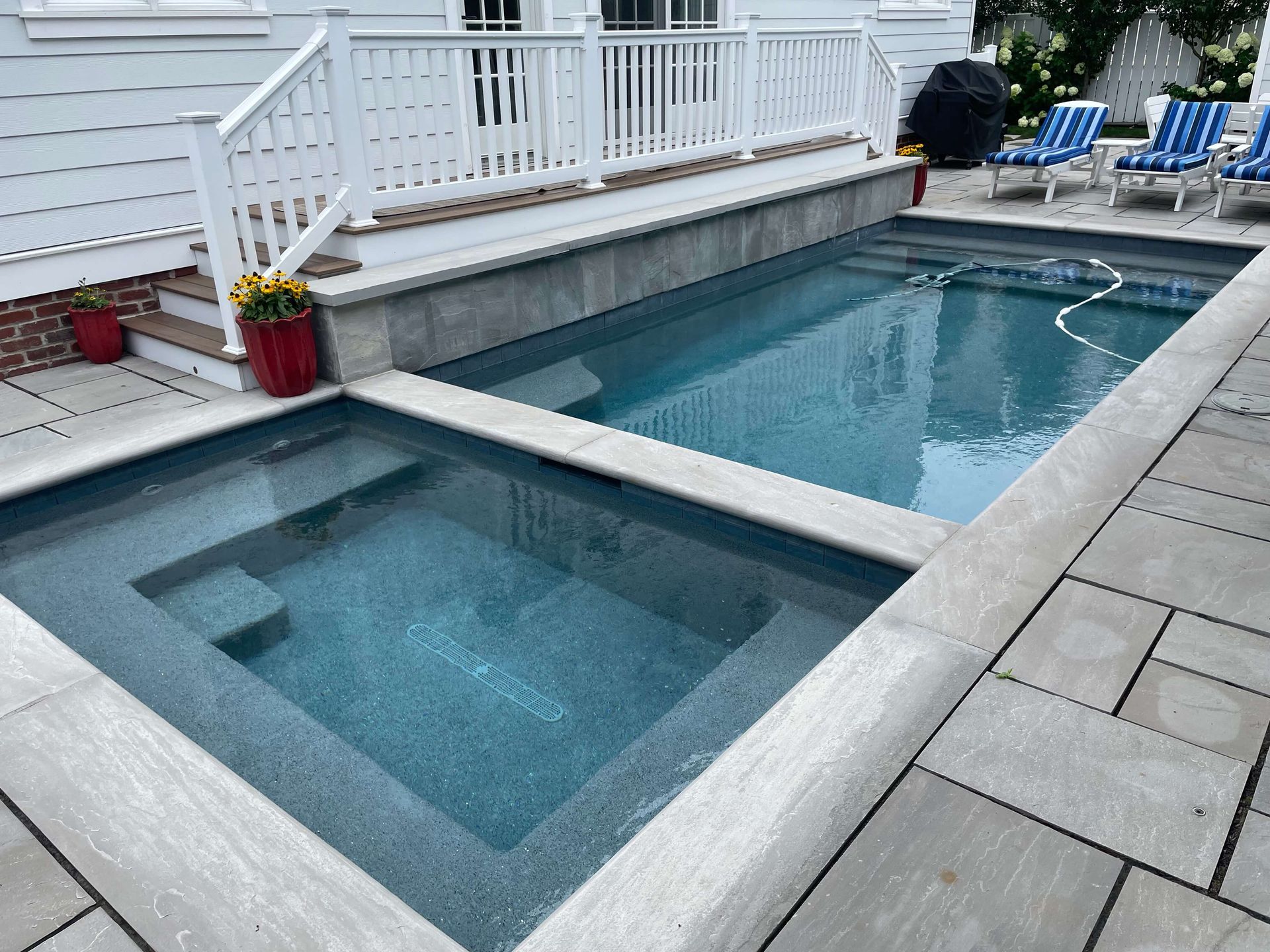 Modern backyard pool with attached hot tub, white deck railings, and blue lounge chairs