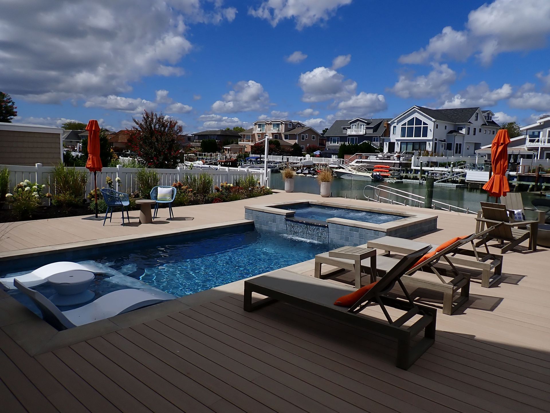 Backyard pool with lounge chairs, umbrellas, and waterfront homes under a blue sky