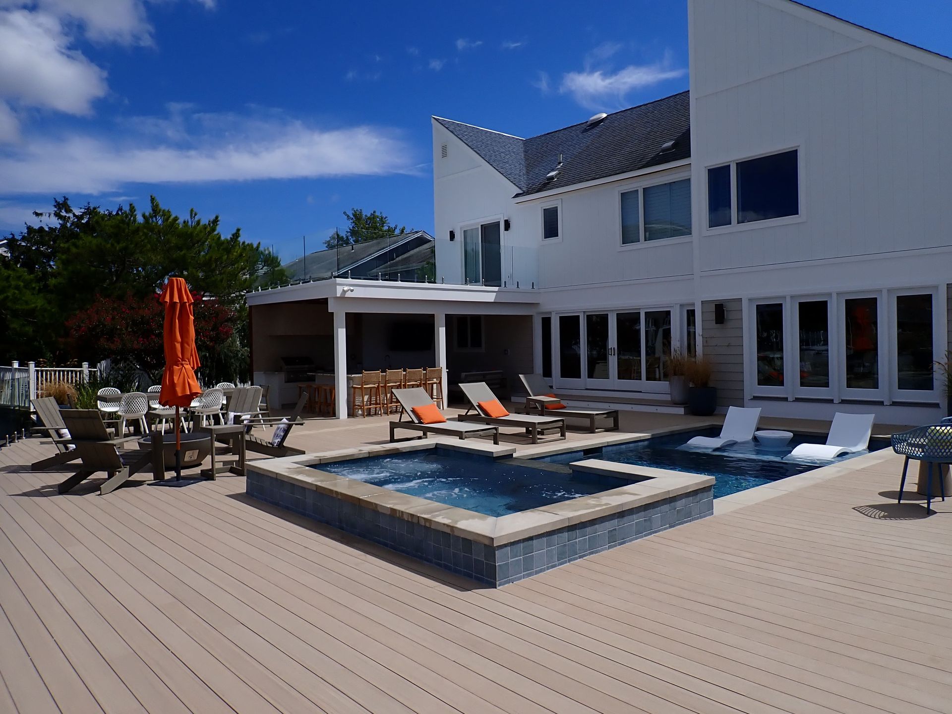 Modern backyard patio with a small pool, lounge chairs, umbrella, and a white house under a blue sky