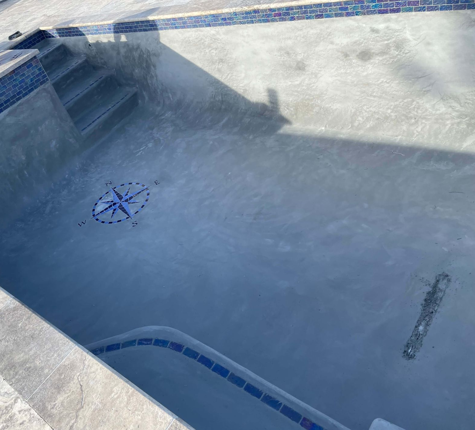 Empty swimming pool with blue tile trim, stairs, and a drain in bright sunlight