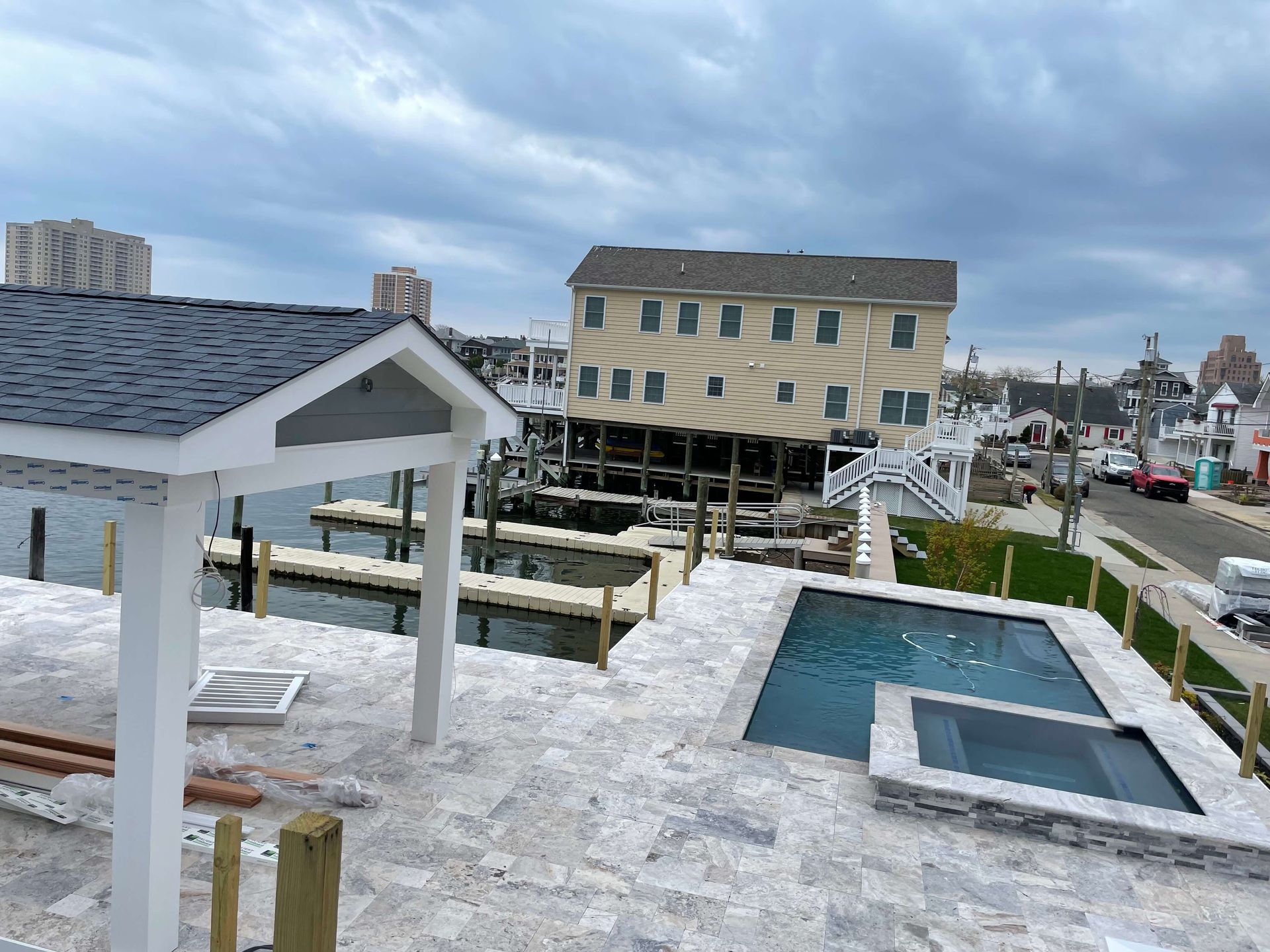 Snowy rooftop deck with white railings, hot tubs, and a seaside town under cloudy skies