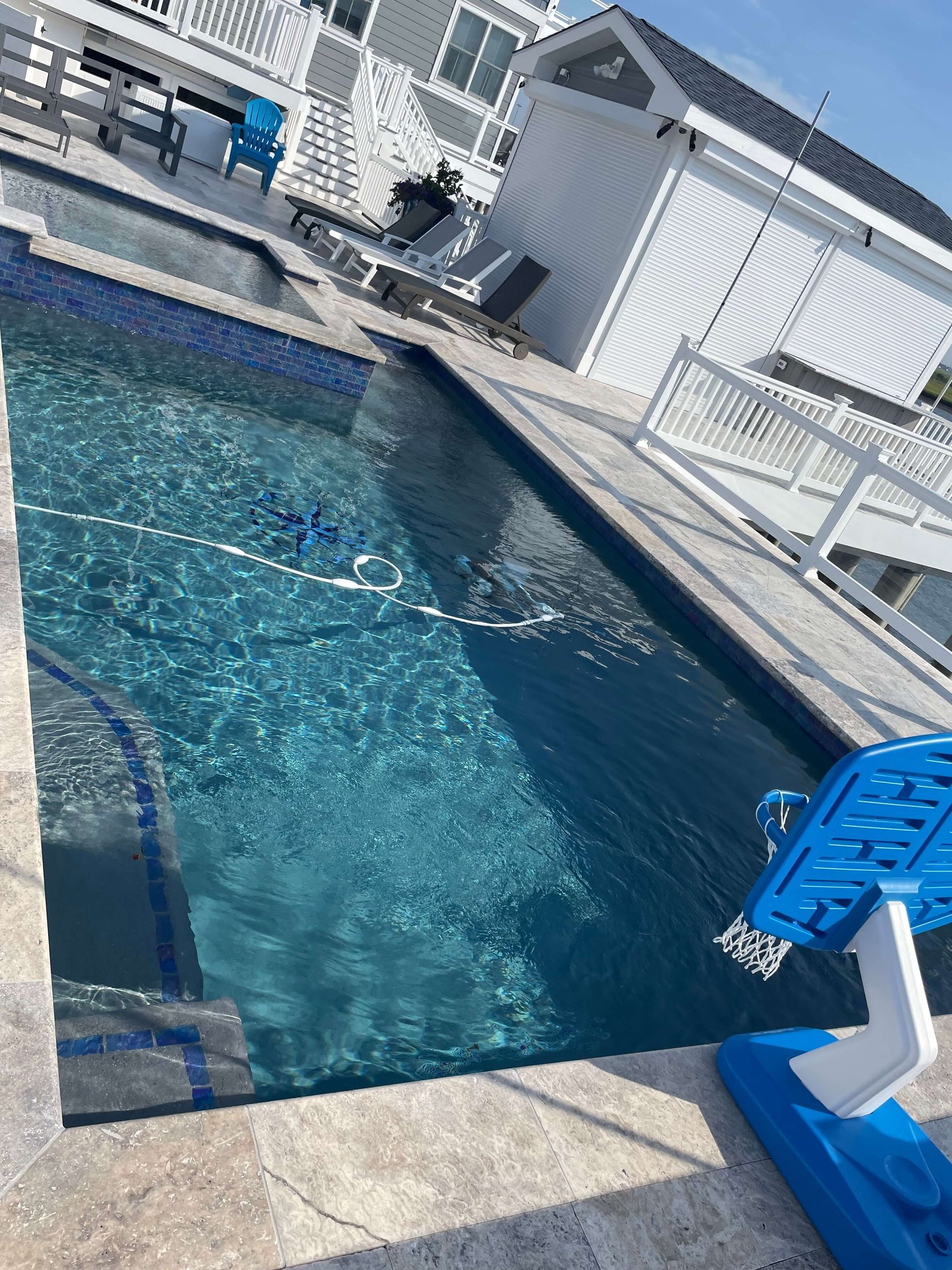 Blue swimming pool beside a white deck and shed, with a blue chair in the foreground.