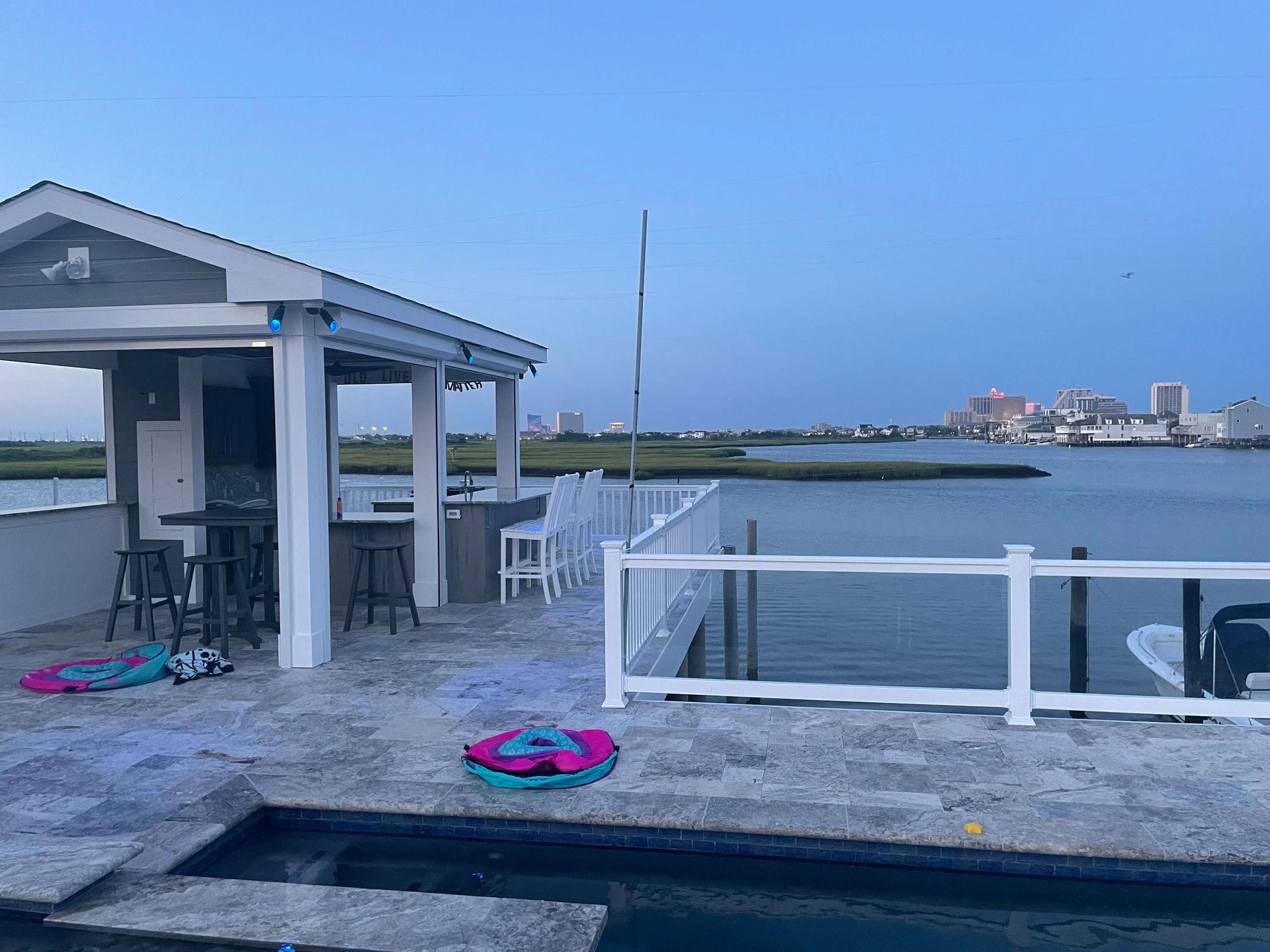 Waterfront patio with white gazebo, colorful float rings, and a calm bay view at dusk.