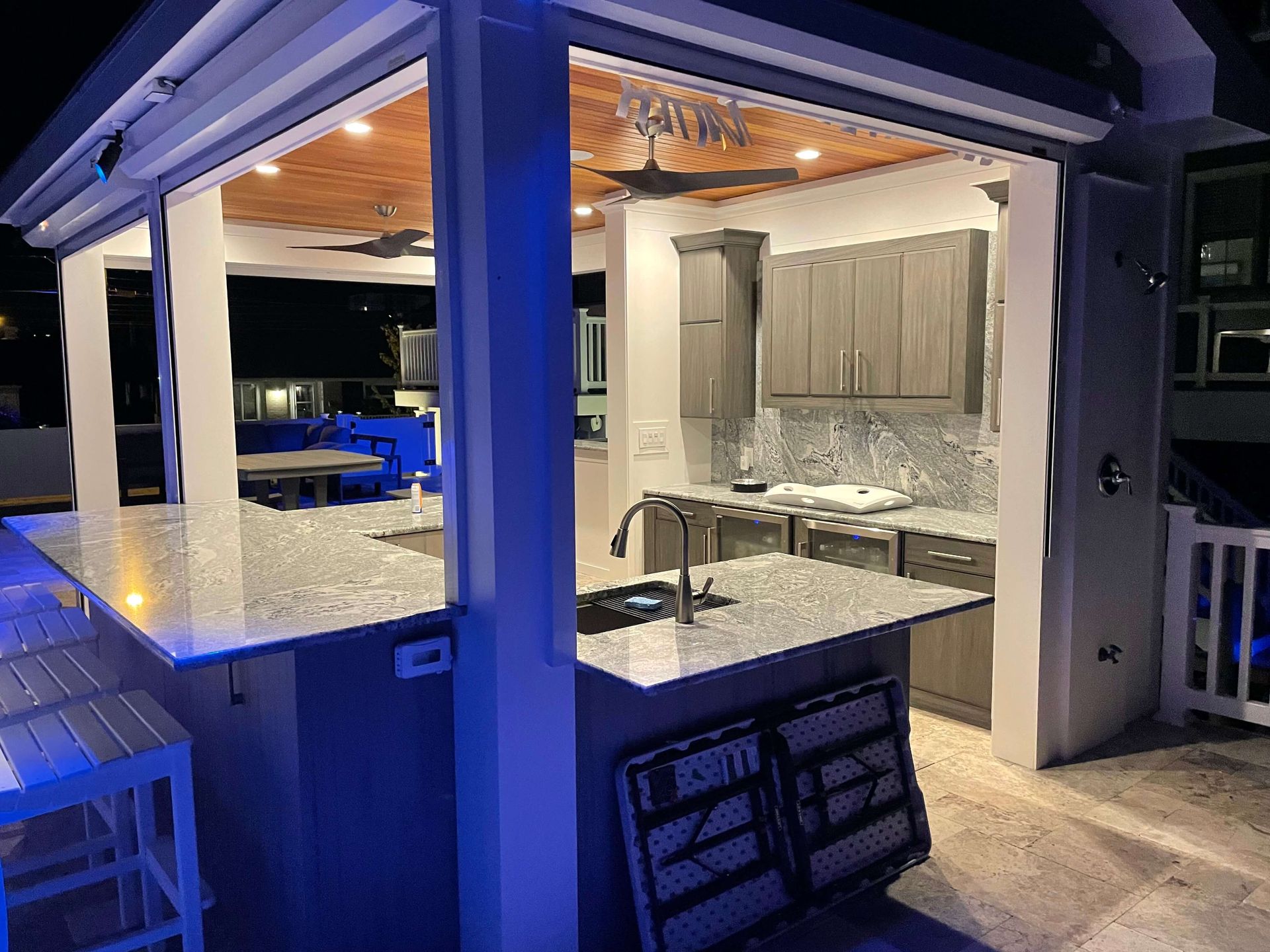 Outdoor patio kitchen with granite counter, cabinets, and blue accent lighting at night