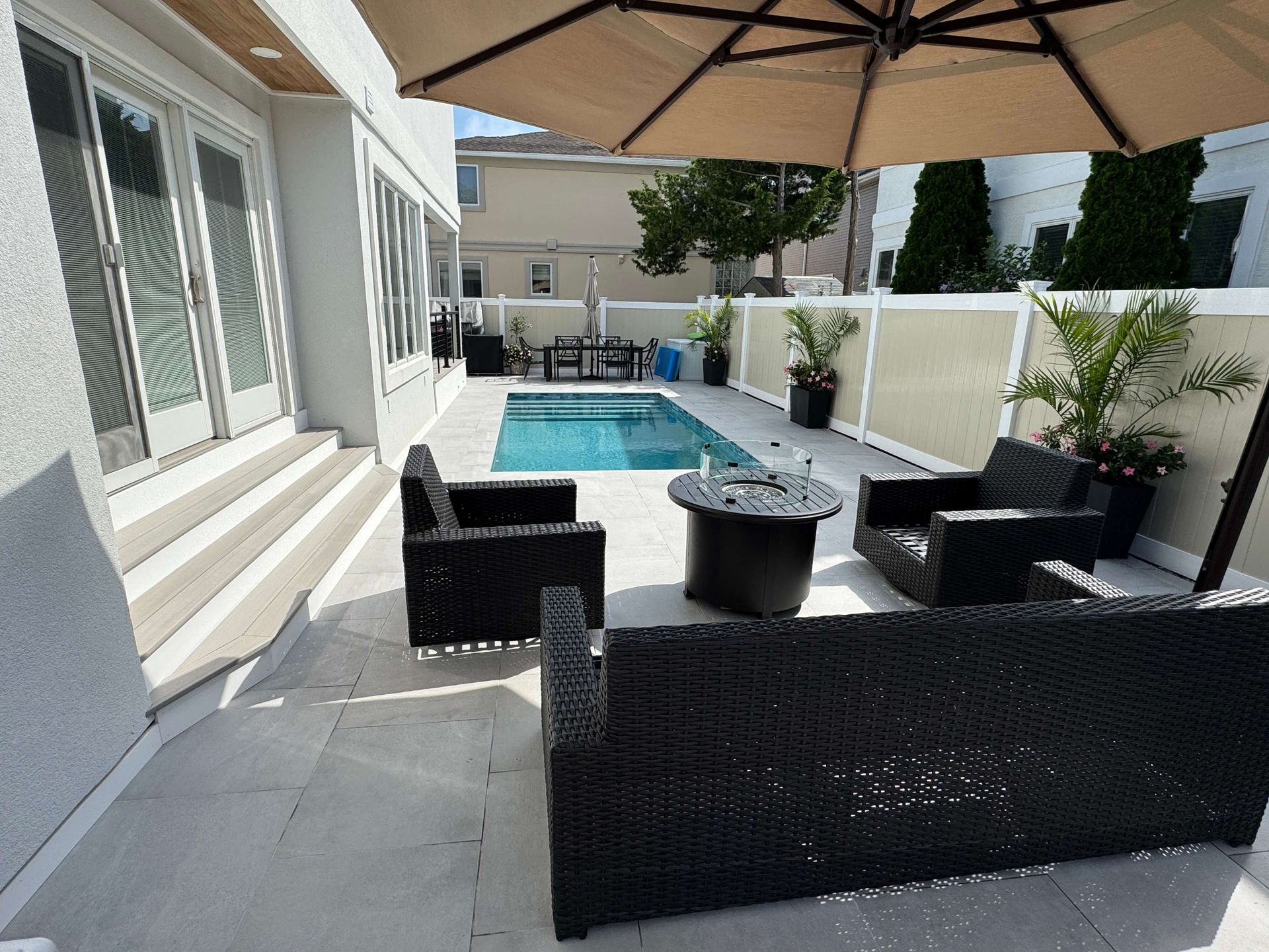 Patio with black wicker seating around a fire pit beside a small backyard pool and sliding doors