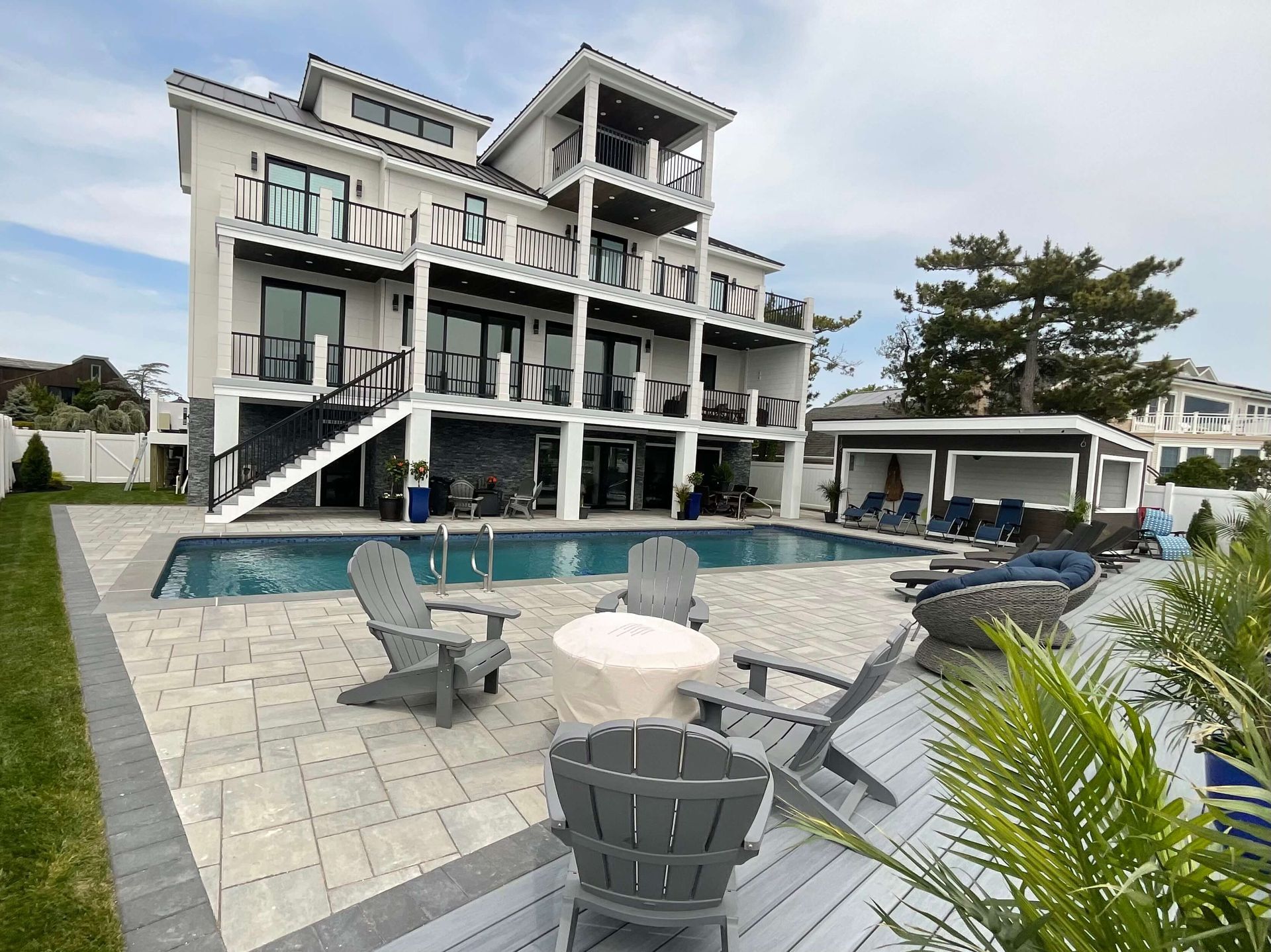 Modern beachfront villa with pool, lounge chairs, and patio seating under a cloudy sky