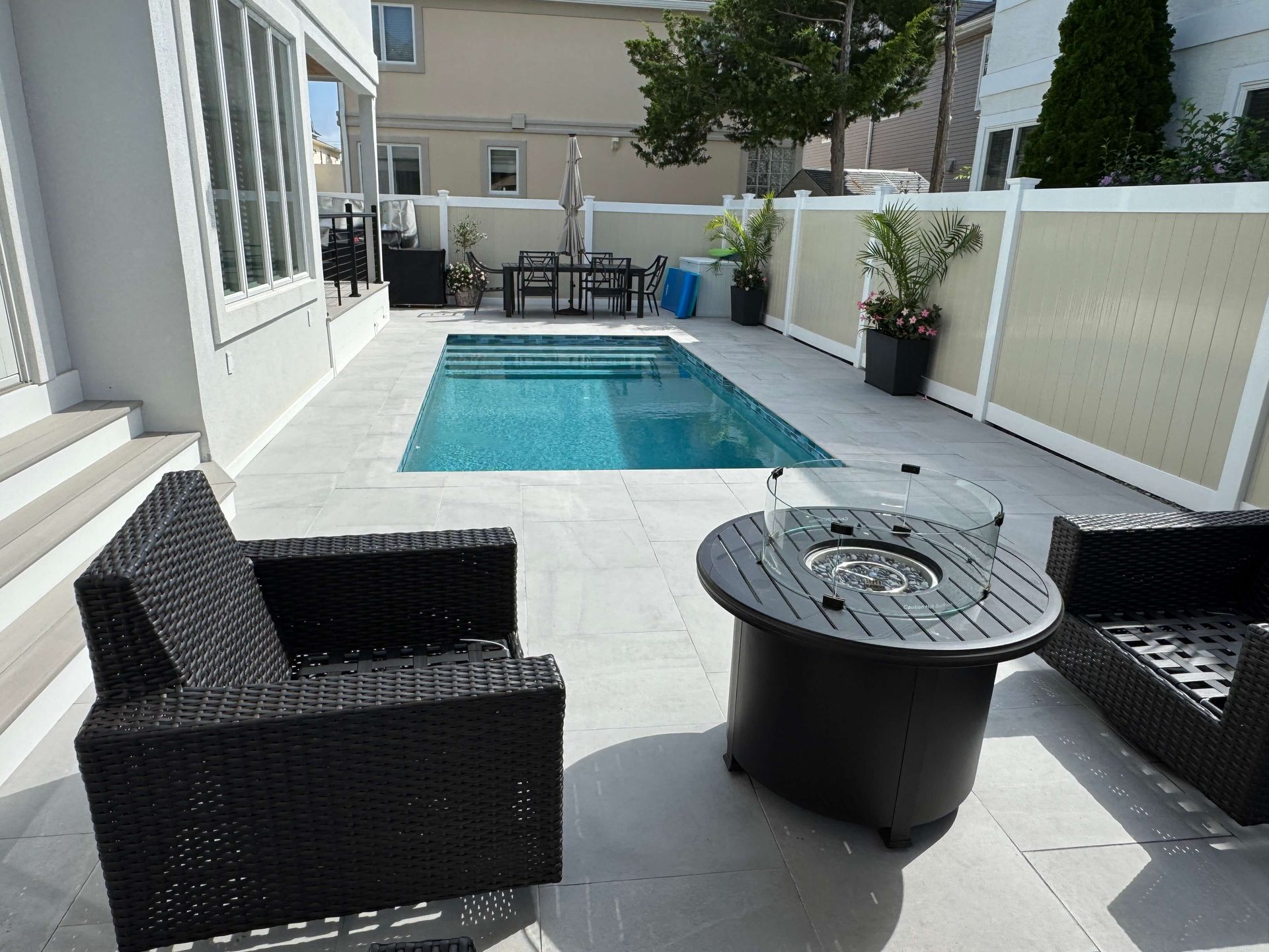 Patio with black wicker chairs and a round table beside a small backyard pool