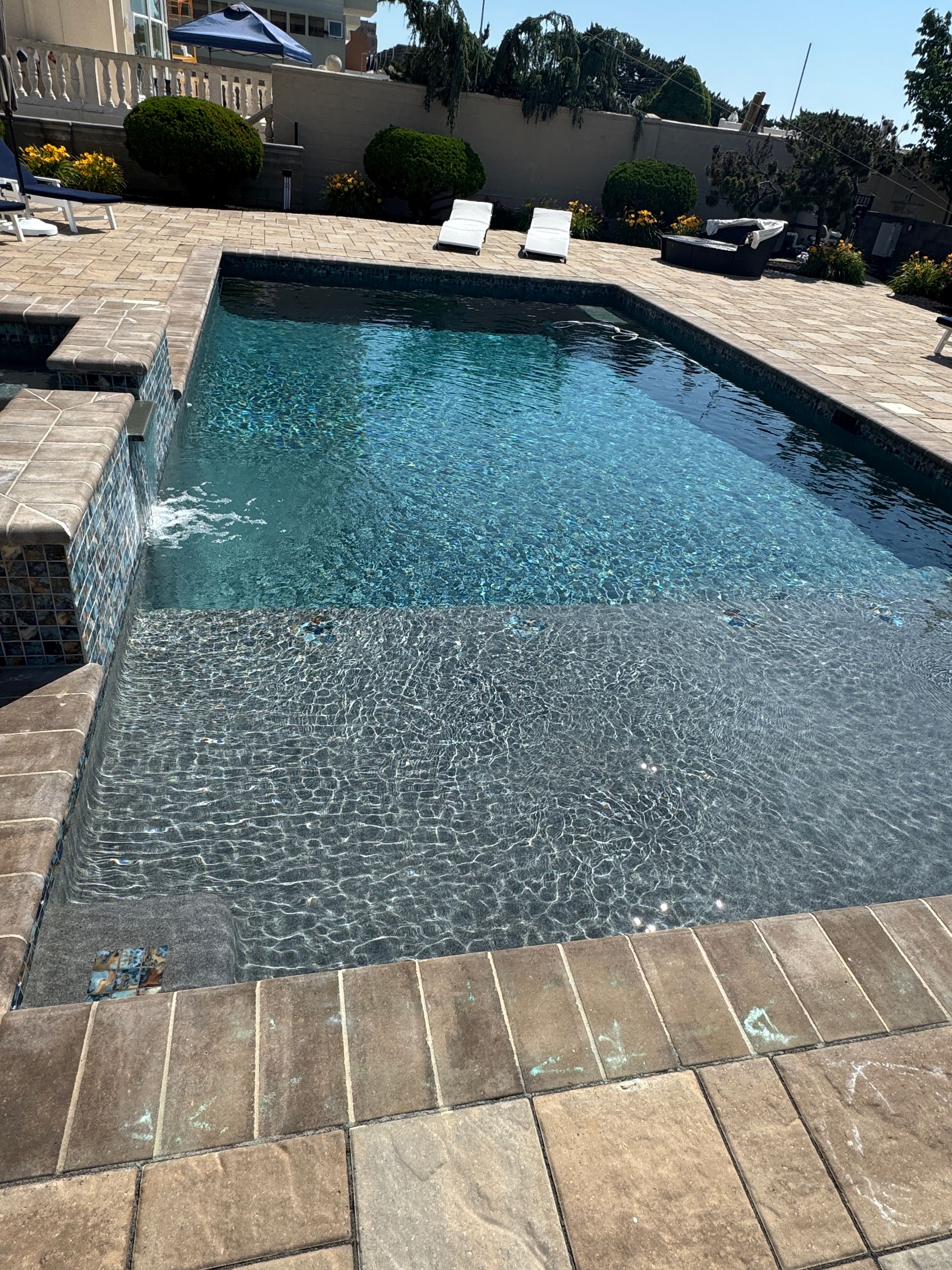 Backyard swimming pool with rippling blue water, stone deck, and two lounge chairs in the background