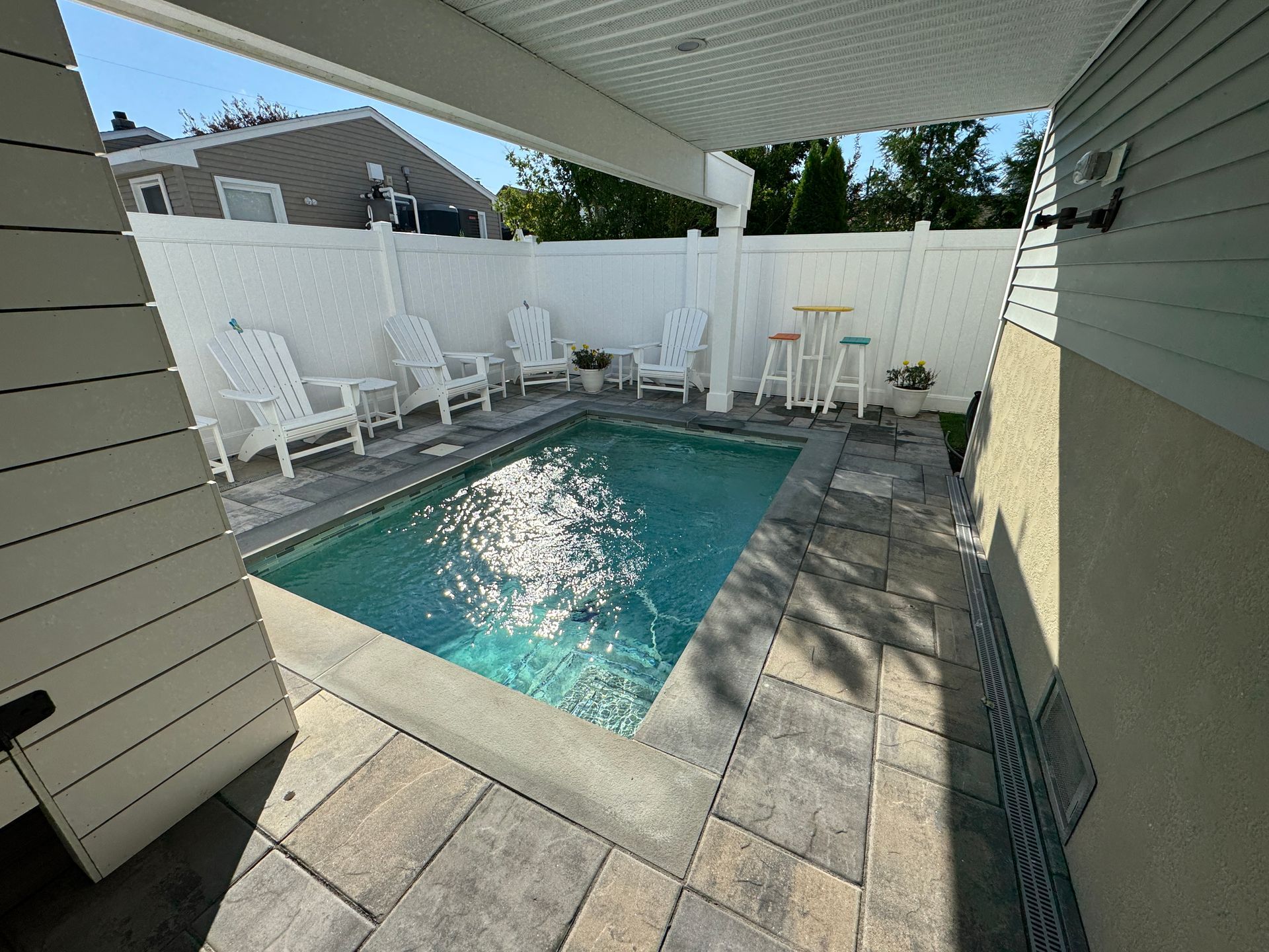 Small backyard patio with a blue swimming pool, white fence, and lounge chairs in shade