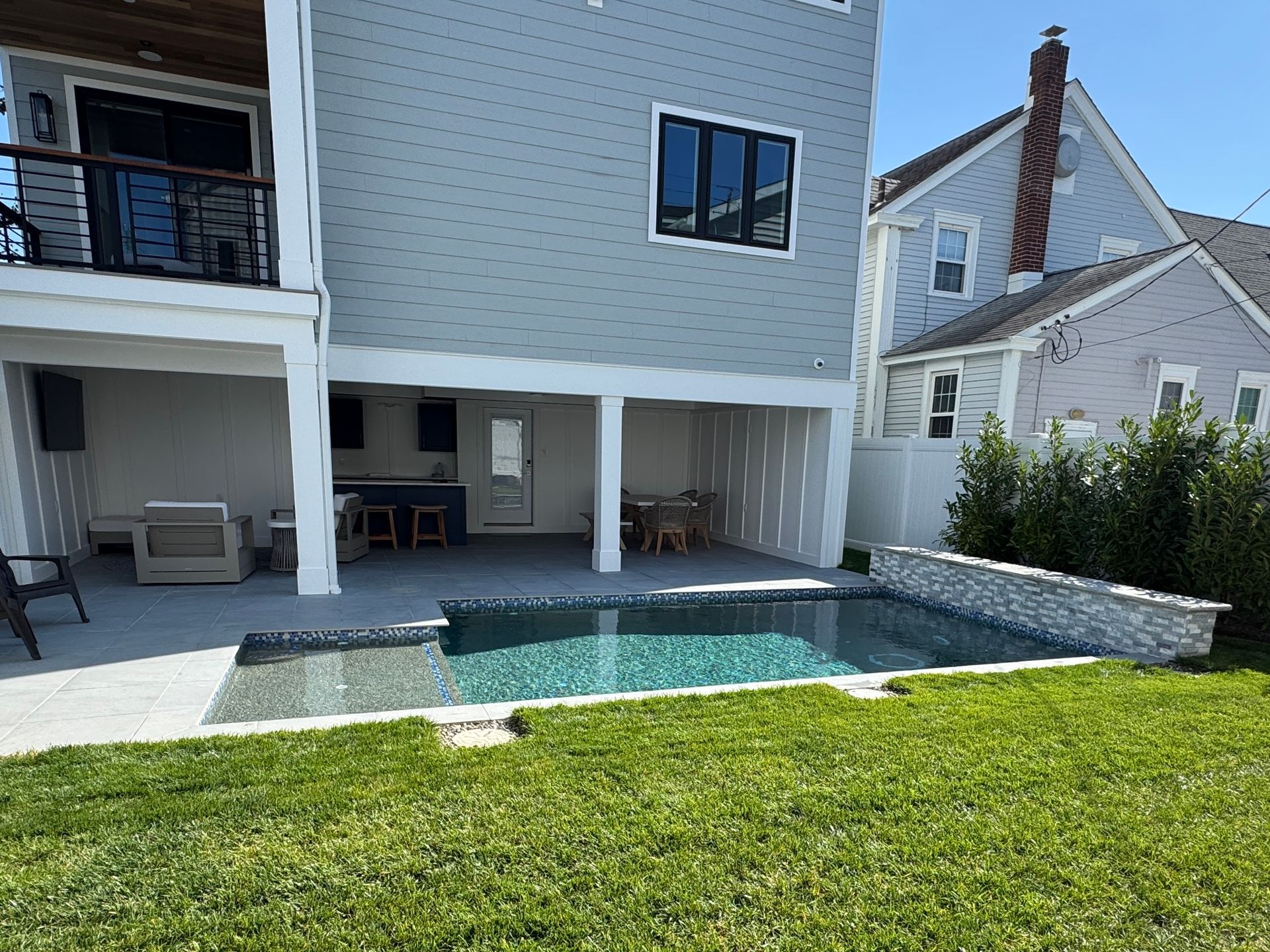 Backyard patio with a small pool, covered seating area, and green lawn beside a modern house