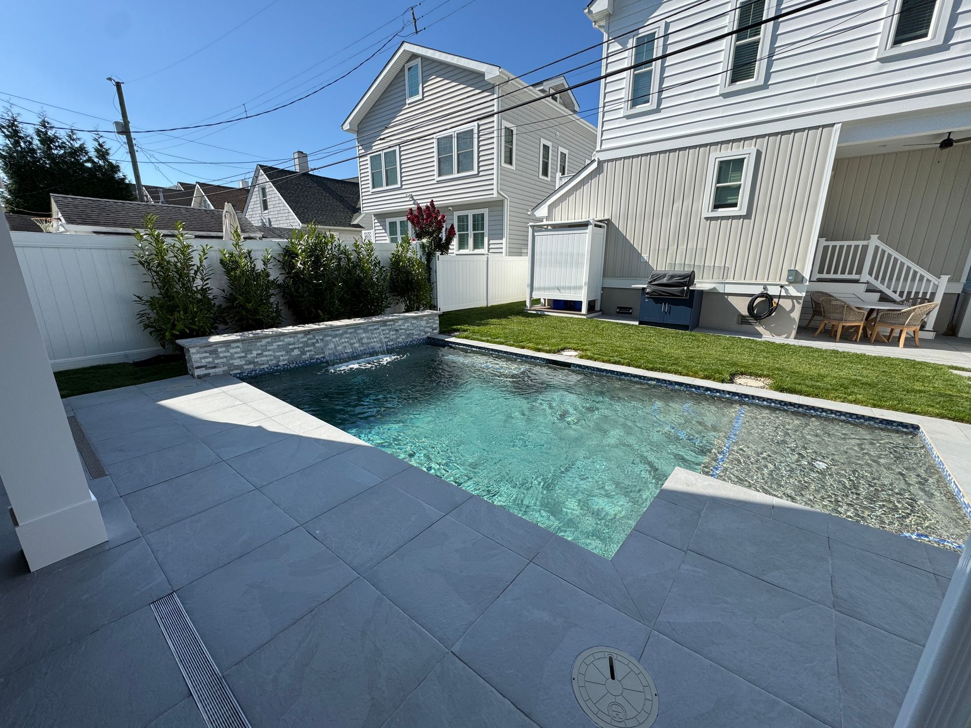 Backyard pool with turquoise water, white pavers, and a modern house beside a small gravel patio