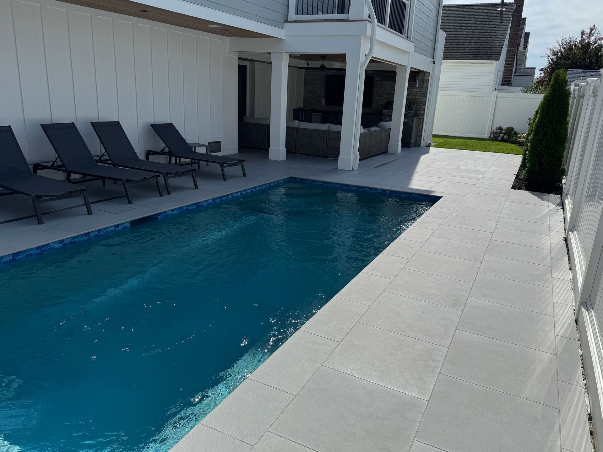 Backyard pool beside a white house with gray deck and lounge chairs
