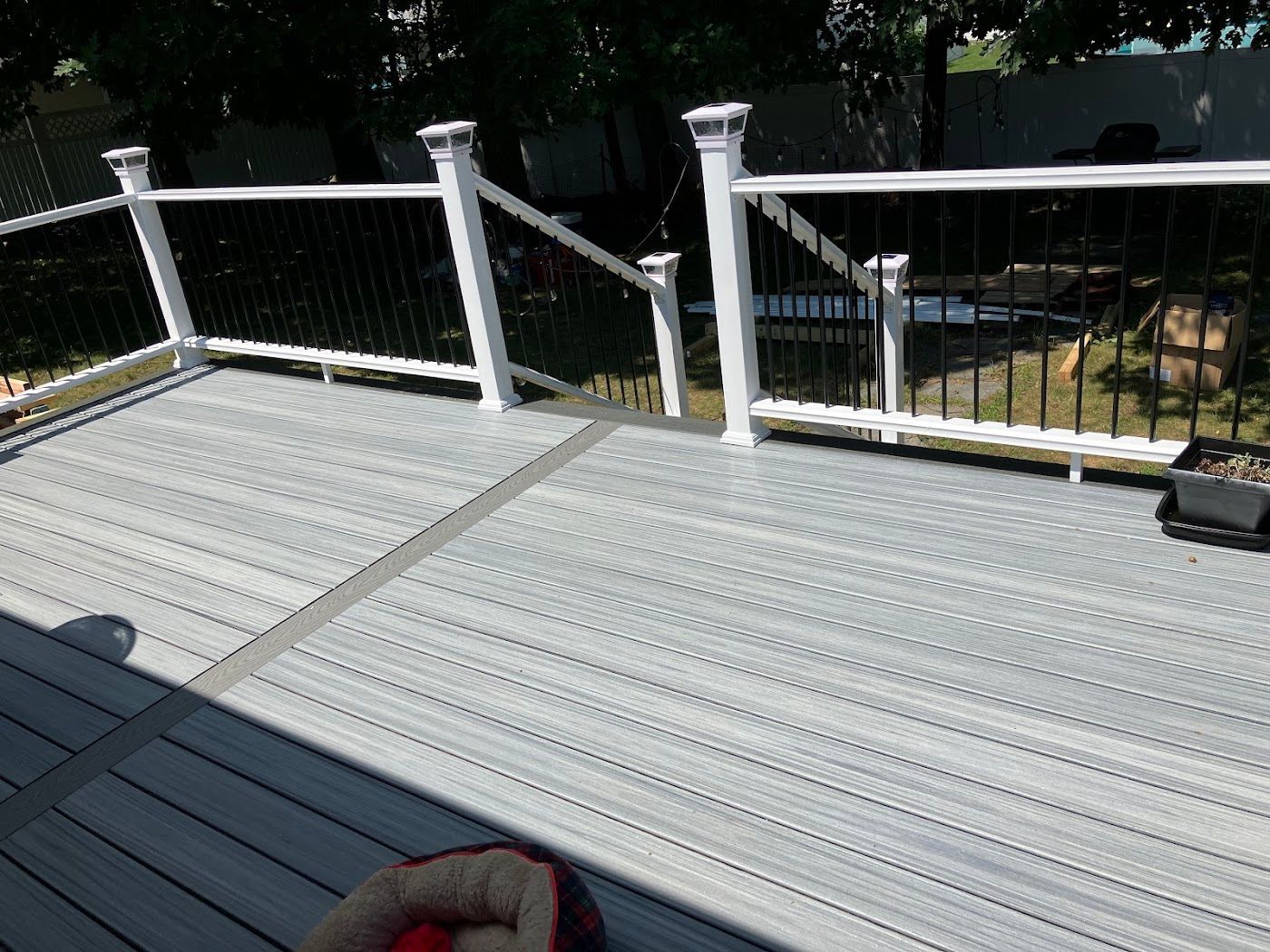 White deck railing beside a gray metal roof, overlooking a yard with trees and a bench
