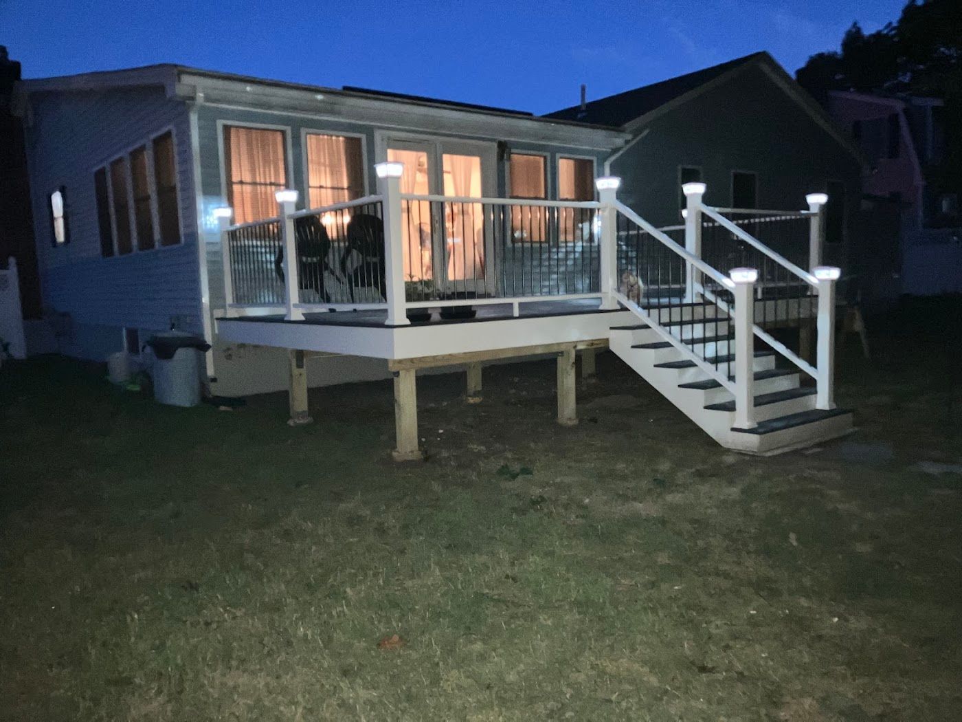 Small illuminated porch with white railings and stairs on a raised house at night.
