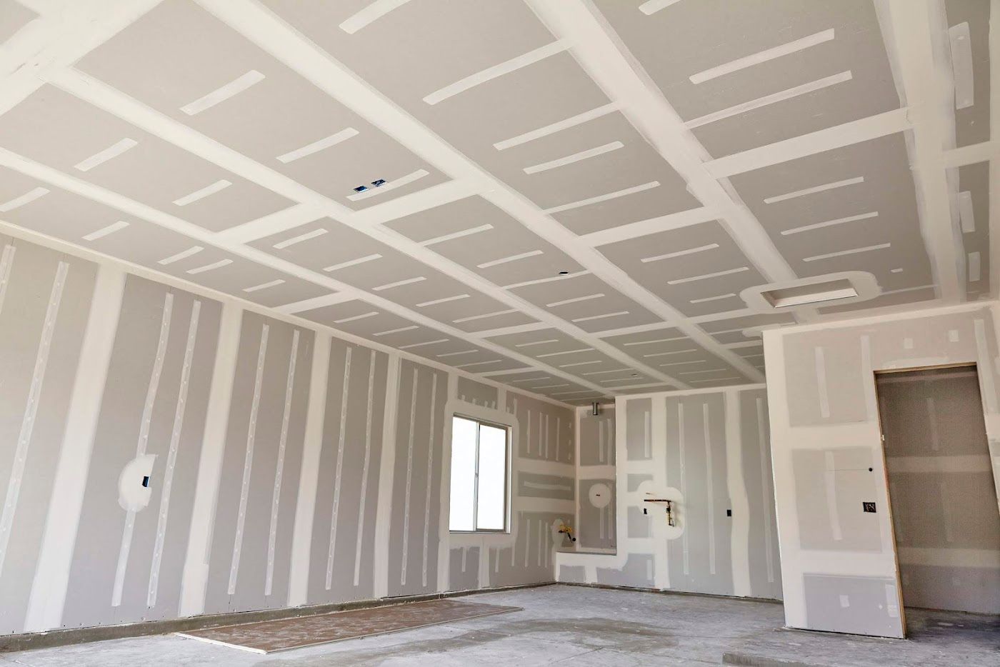 Unfinished drywall room with taped seams, a window, and an open doorway in a bright interior