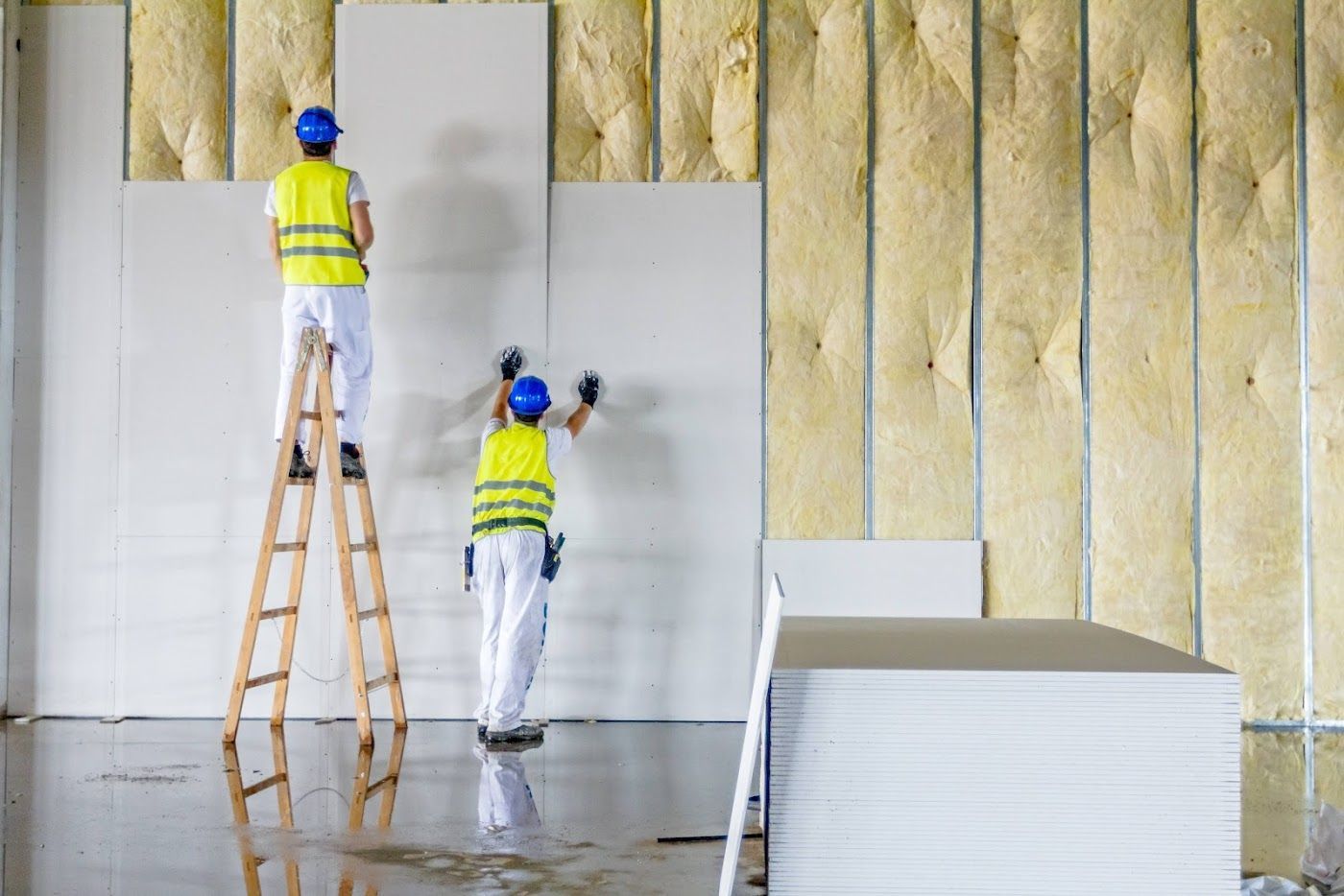 Two workers insulating and painting a wall inside a building under construction